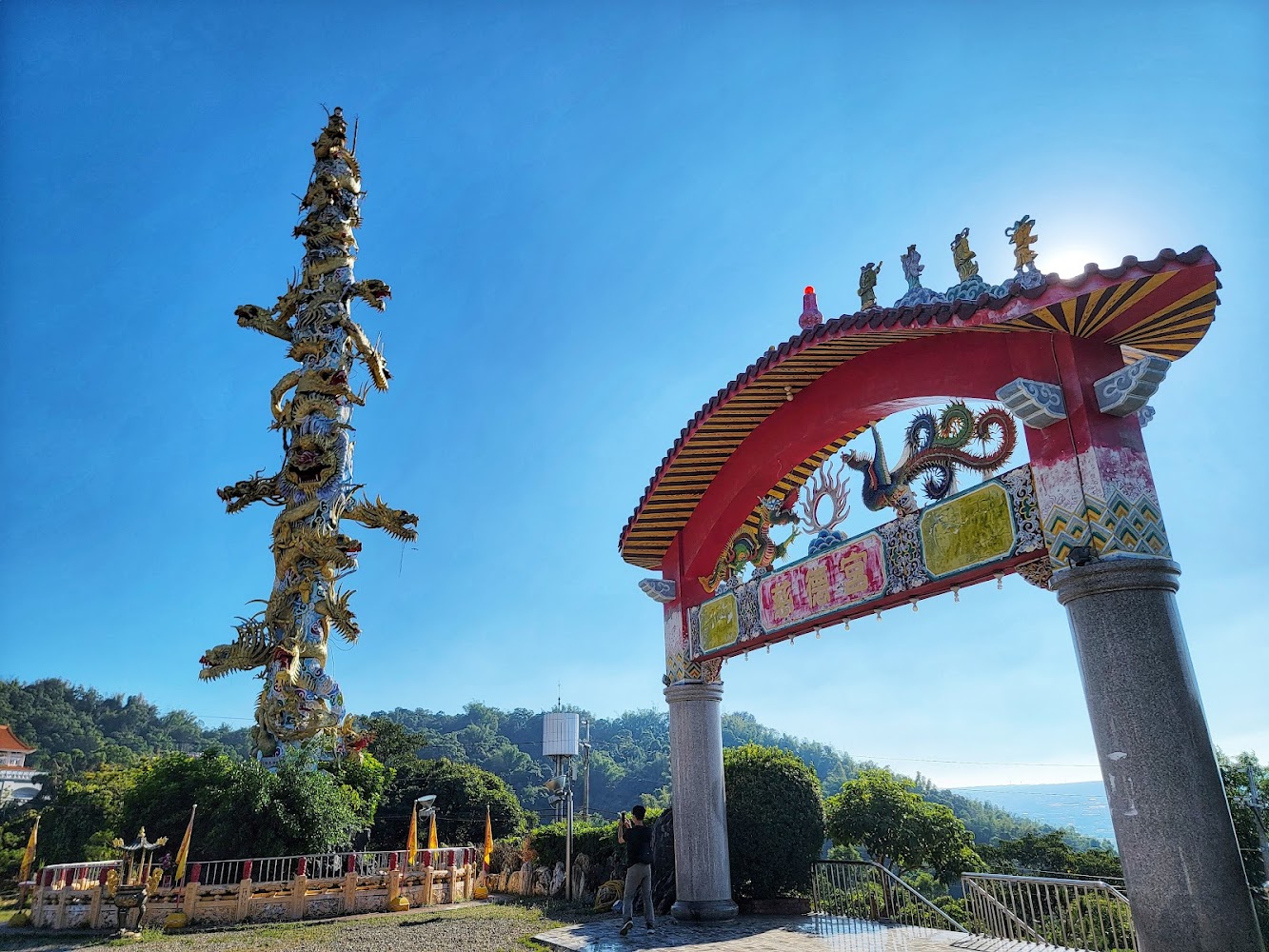 中式牌樓旁高聳龍柱，背景有藍天與山景