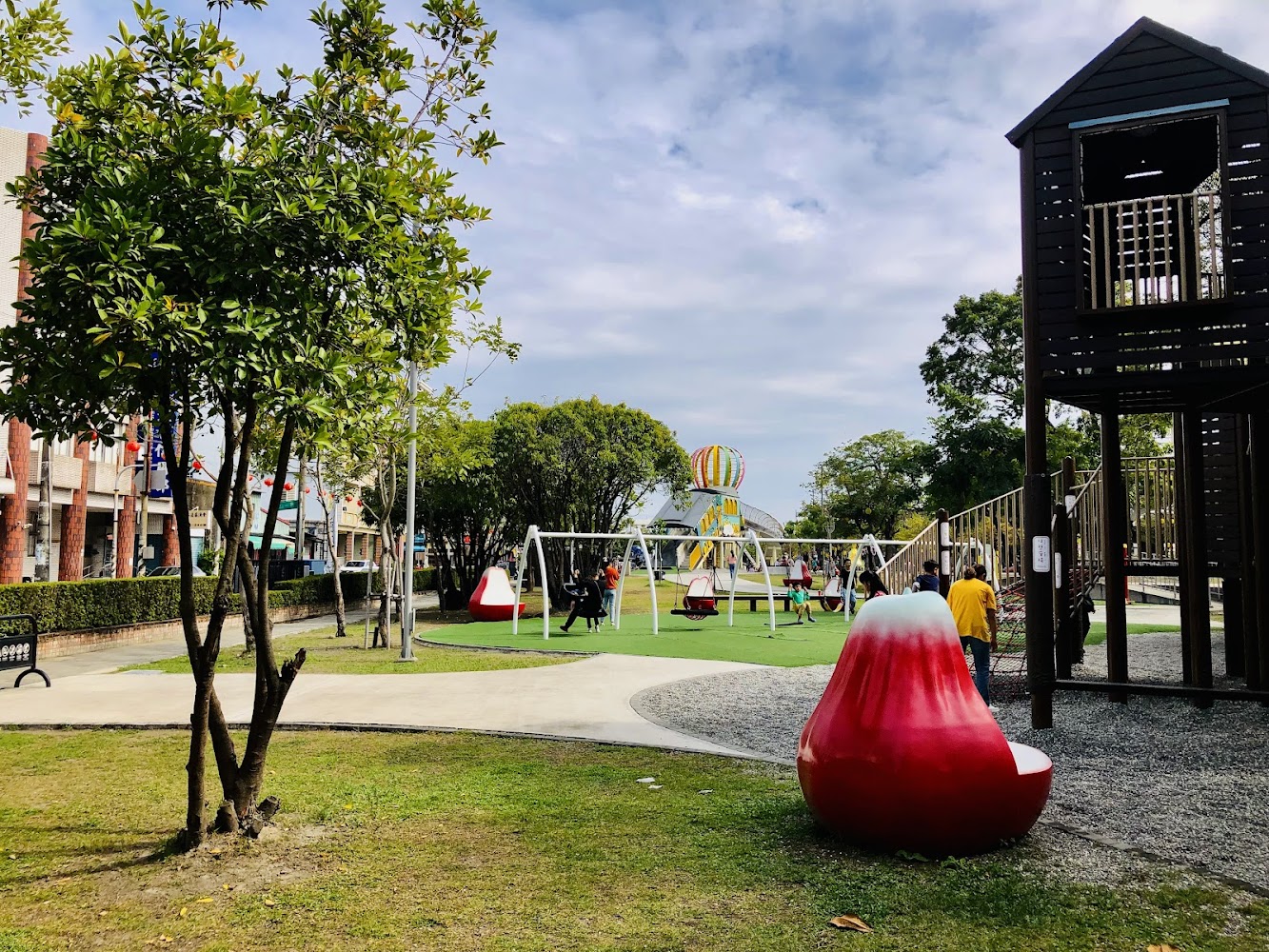 這是一個公園遊樂場,有盪鞦韆、溜滑梯和攀爬設施,還有特色紅色椅子和熱氣球裝飾,適合小朋友玩耍。
