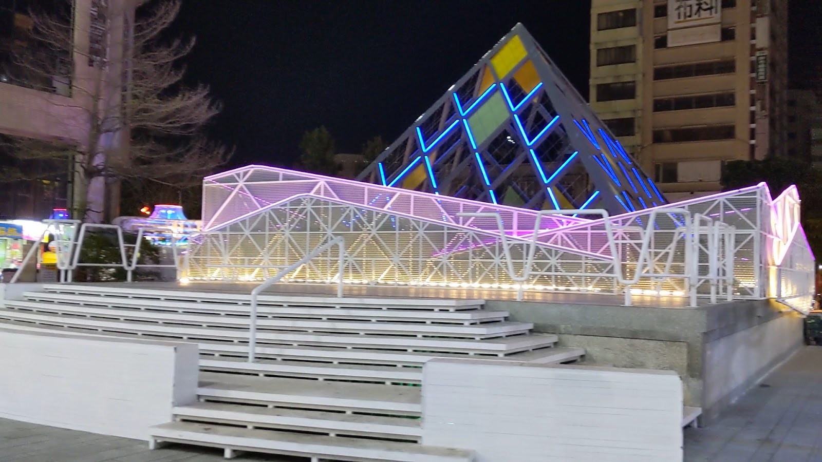 台中東協廣場入口玻璃金字塔裝置藝術夜景，七彩霓虹燈光點亮幾何鋼構天棚