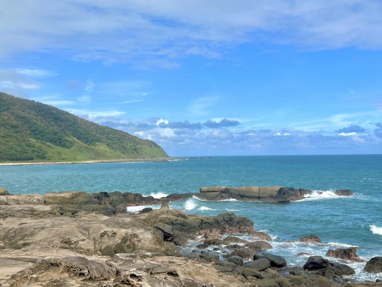 佳樂水風景區全景,左側綠色山丘,前方海蝕礁岩,碧藍太平洋與藍天白雲