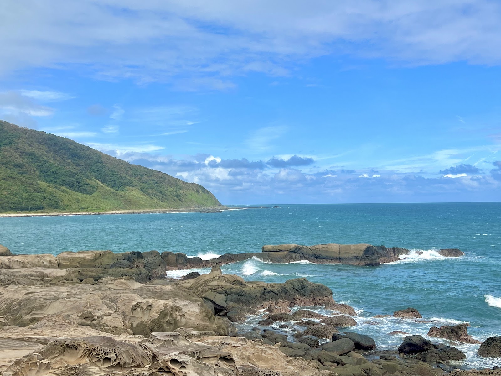 佳樂水風景區全景,左側綠色山丘,前方海蝕礁岩,碧藍太平洋與藍天白雲