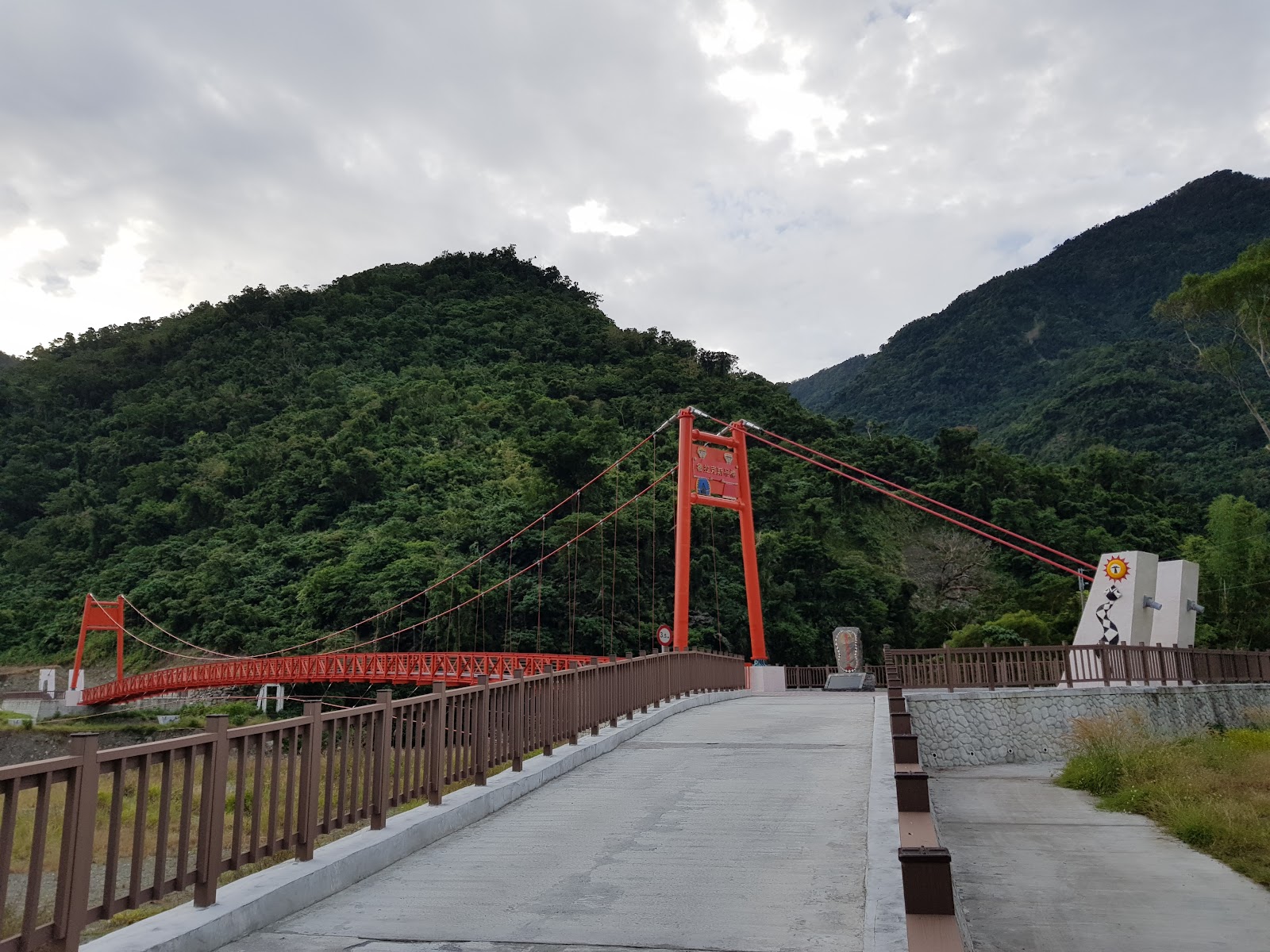 台東金峰鄉魯拉克斯吊橋橙紅色橋面，棕色護欄，背景翠綠山巒