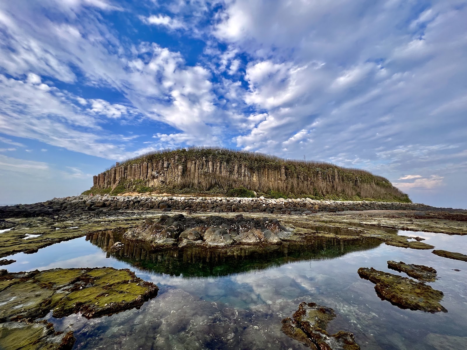澎湖桶盤嶼柱狀玄武岩全景，整座島被規律玄武岩峭壁環繞，前景潮池倒映藍天