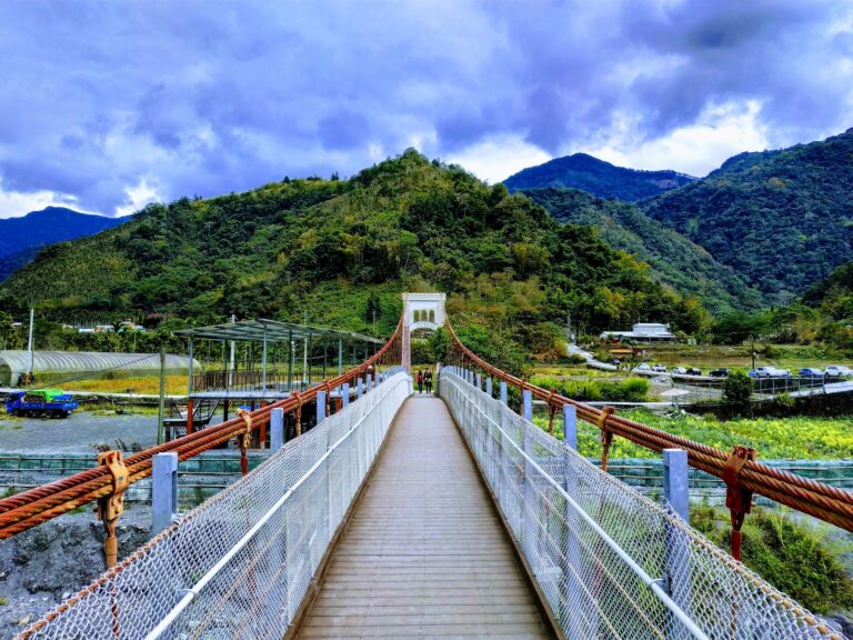 武界吊橋橋面廣角全景,橘紅鋼纜從近端延伸至遠方白色拱門,兩側青山開闊,雲霧繚繞