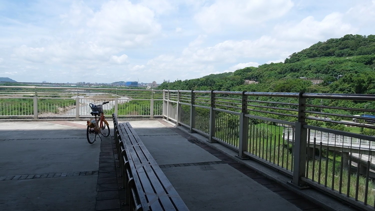 觀景台旁停放一輛公共自行車，遠方有河流、山丘與藍天白雲。