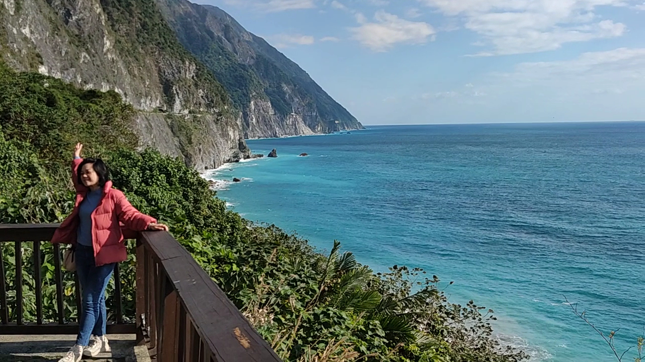 花蓮海岸峭壁與觀景平台，一位穿紅色外套的女子正在賞景