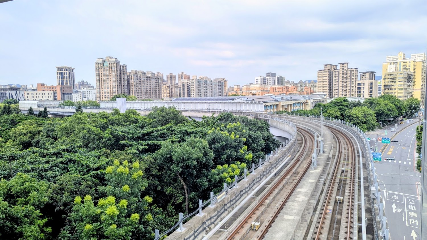 彎曲的高架捷運軌道穿過綠意環境，遠處可見現代高樓。