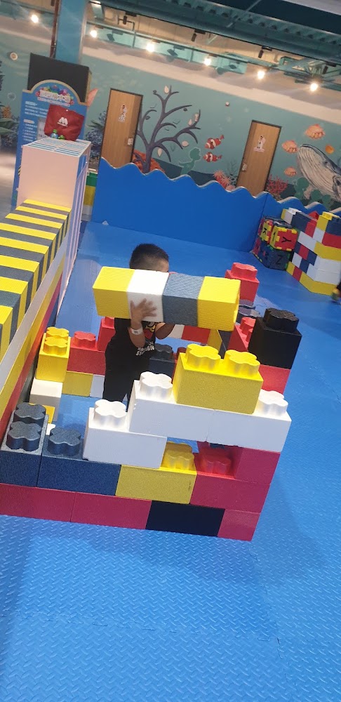 小孩在遊戲區用大型積木堆疊建築物,背景有海洋主題壁畫