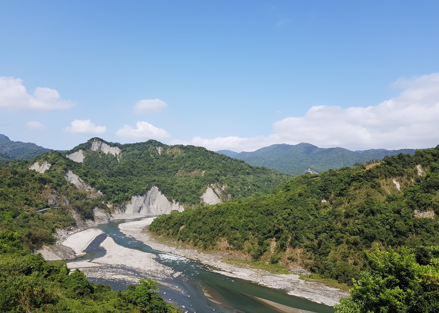 清澈河流蜿蜒穿越花蓮山谷，搭配藍天白雲與綠色山脈