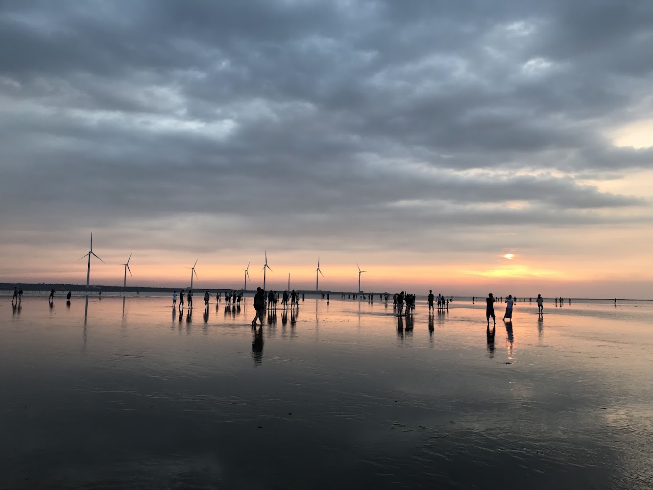 夕陽下濕地漫步人群與風力發電機