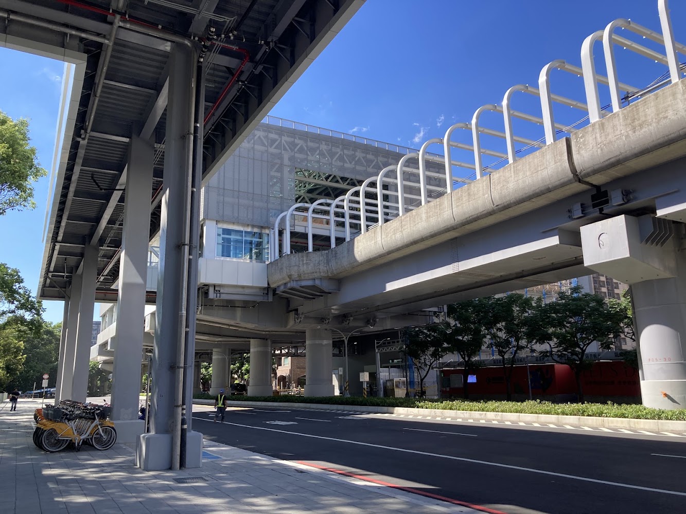三峽站外觀與高架捷運軌道，下方有人行道與共用自行車，天空晴朗。