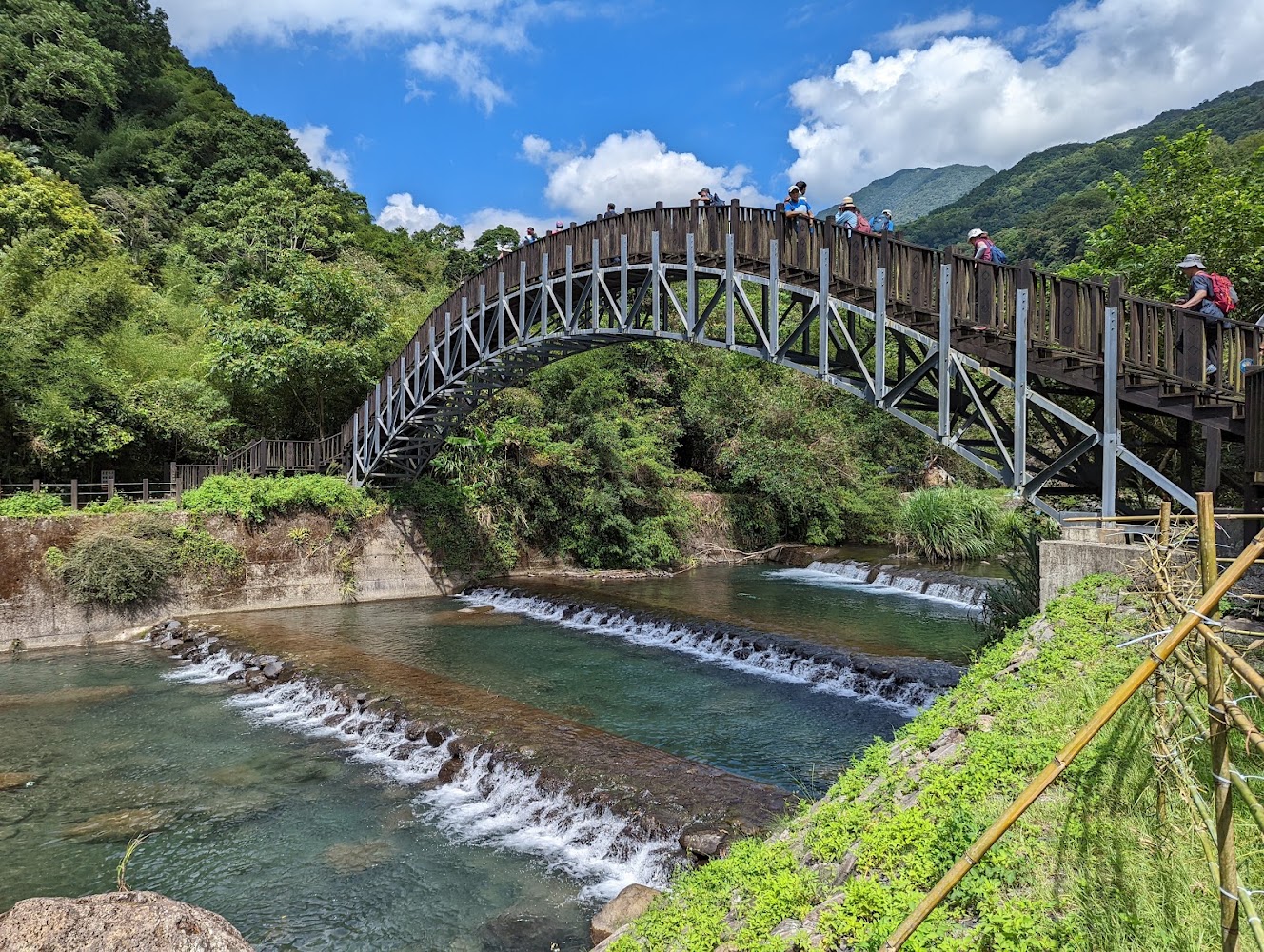 拱形木橋橫跨清澈溪流與山林步道景色