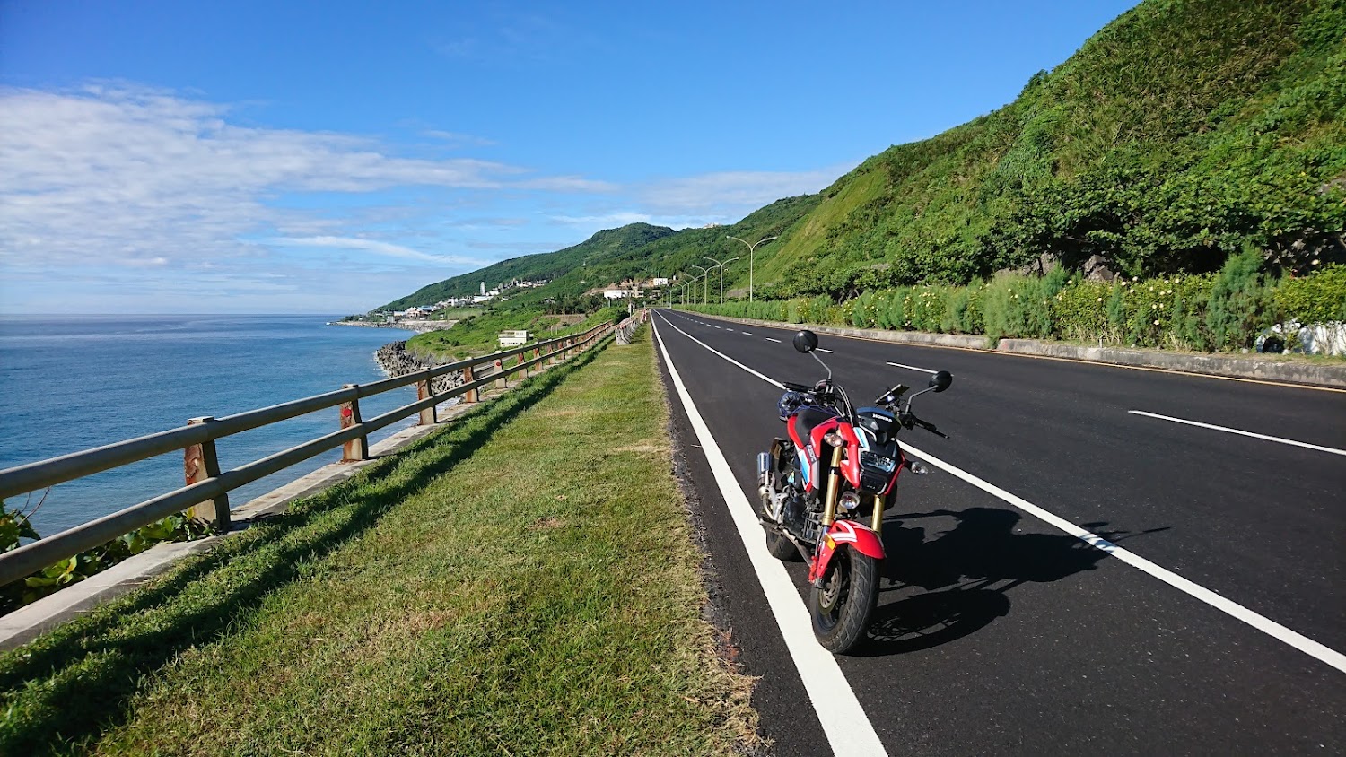 紅色機車停在花蓮海邊公路，左側是藍色海洋，右側是綠色山坡