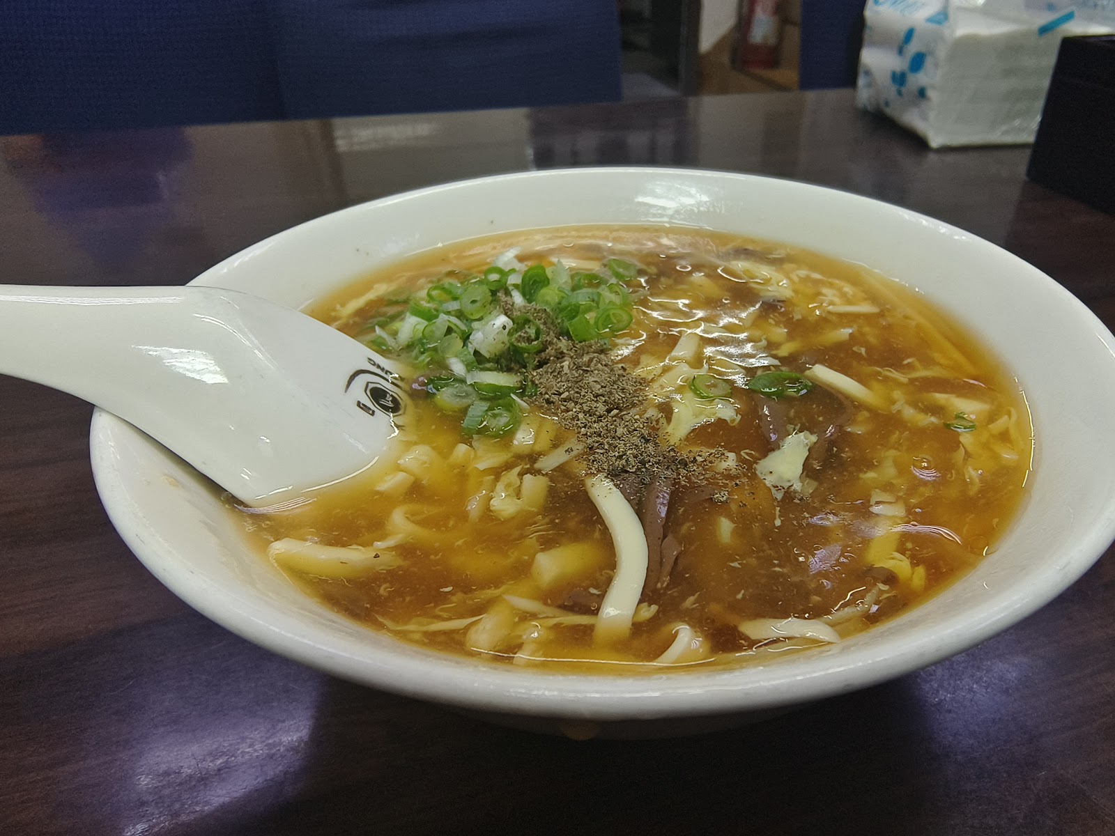 丰清揚小吃店酸辣湯麵，白色寬麵條配濃郁湯頭與蔥花胡椒粉，附白色湯匙