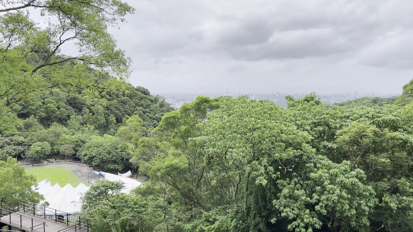 貴子坑水土保持教學園區觀景台俯瞰視角，可見下方露營場草地與遠方台北盆地天際線