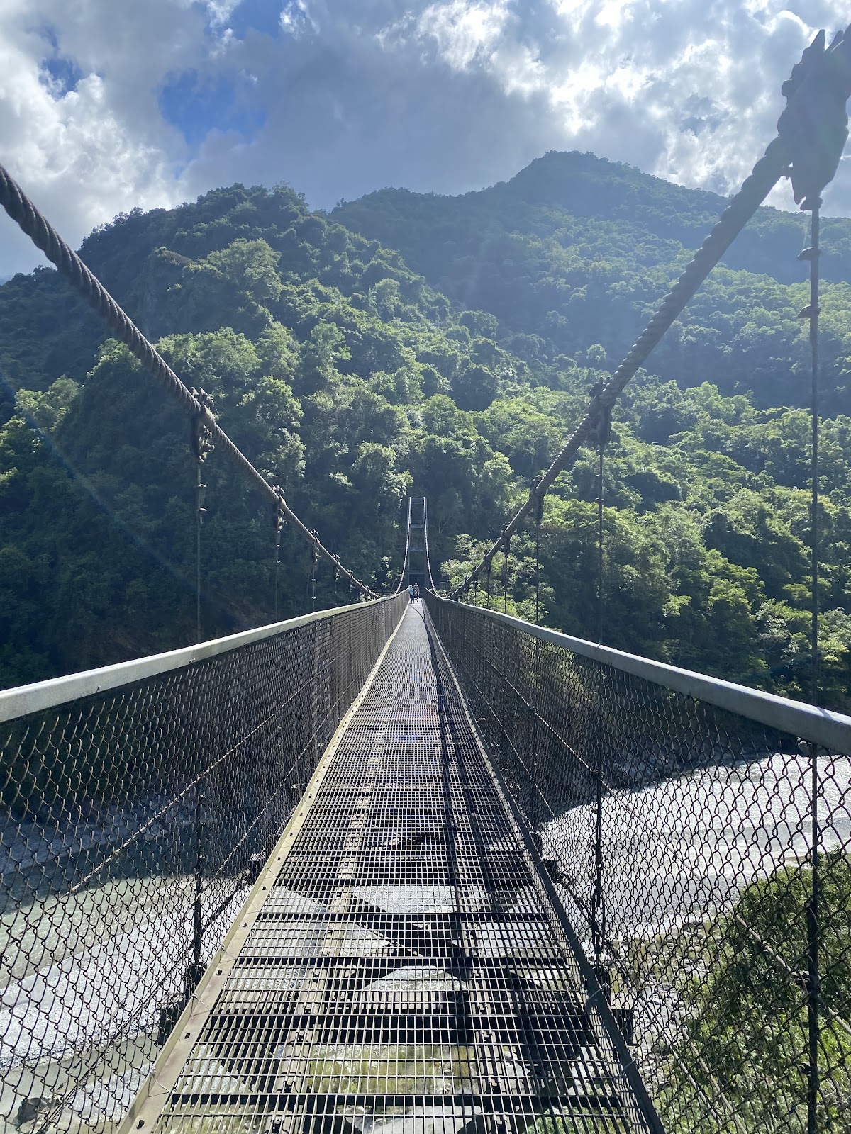 鹿鳴吊橋橋面往前延伸，橋下溪水清澈，兩側山巒環繞