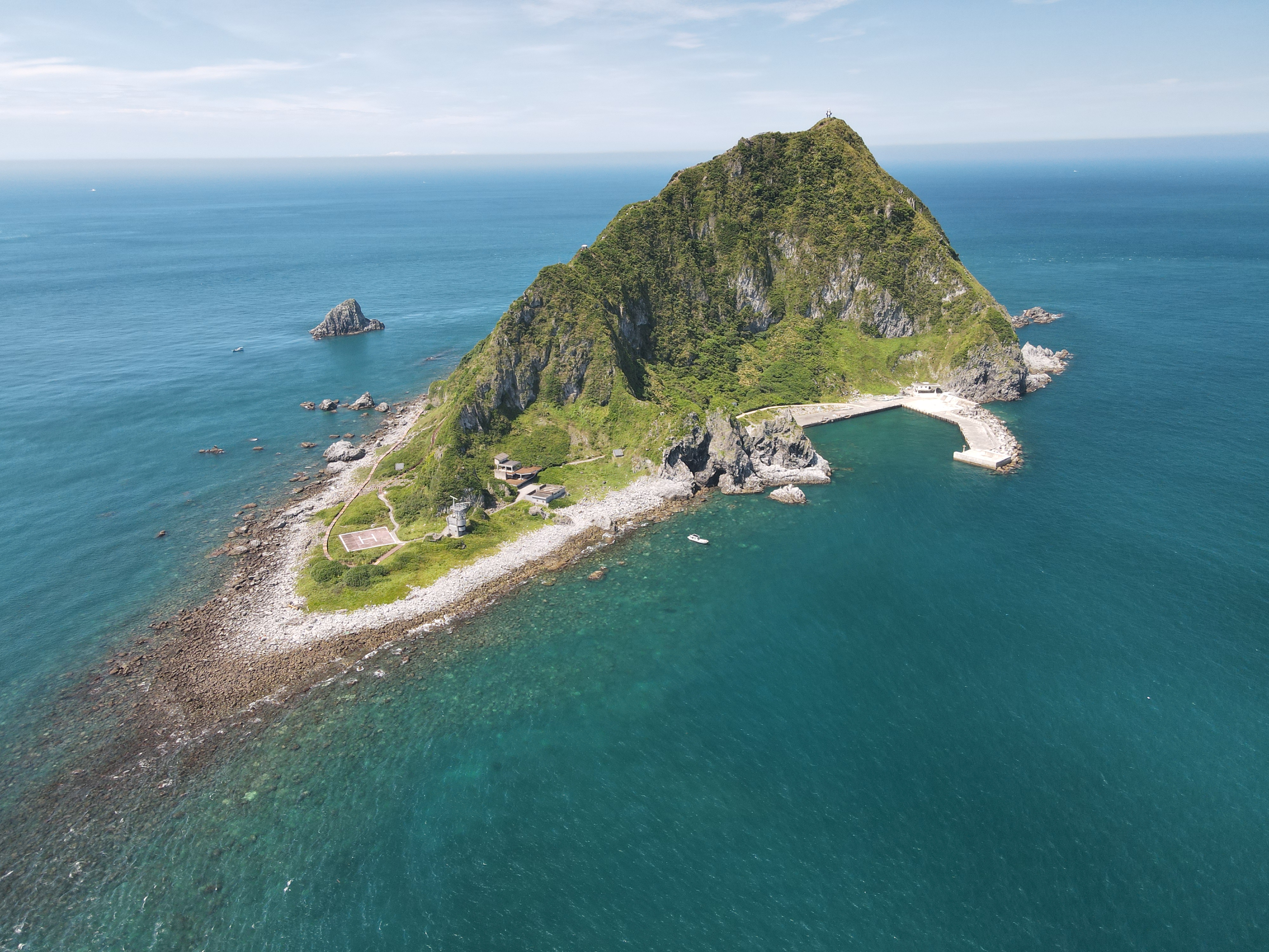 海上遠望基隆嶼全景，綠色山丘與碼頭建築被藍海環繞