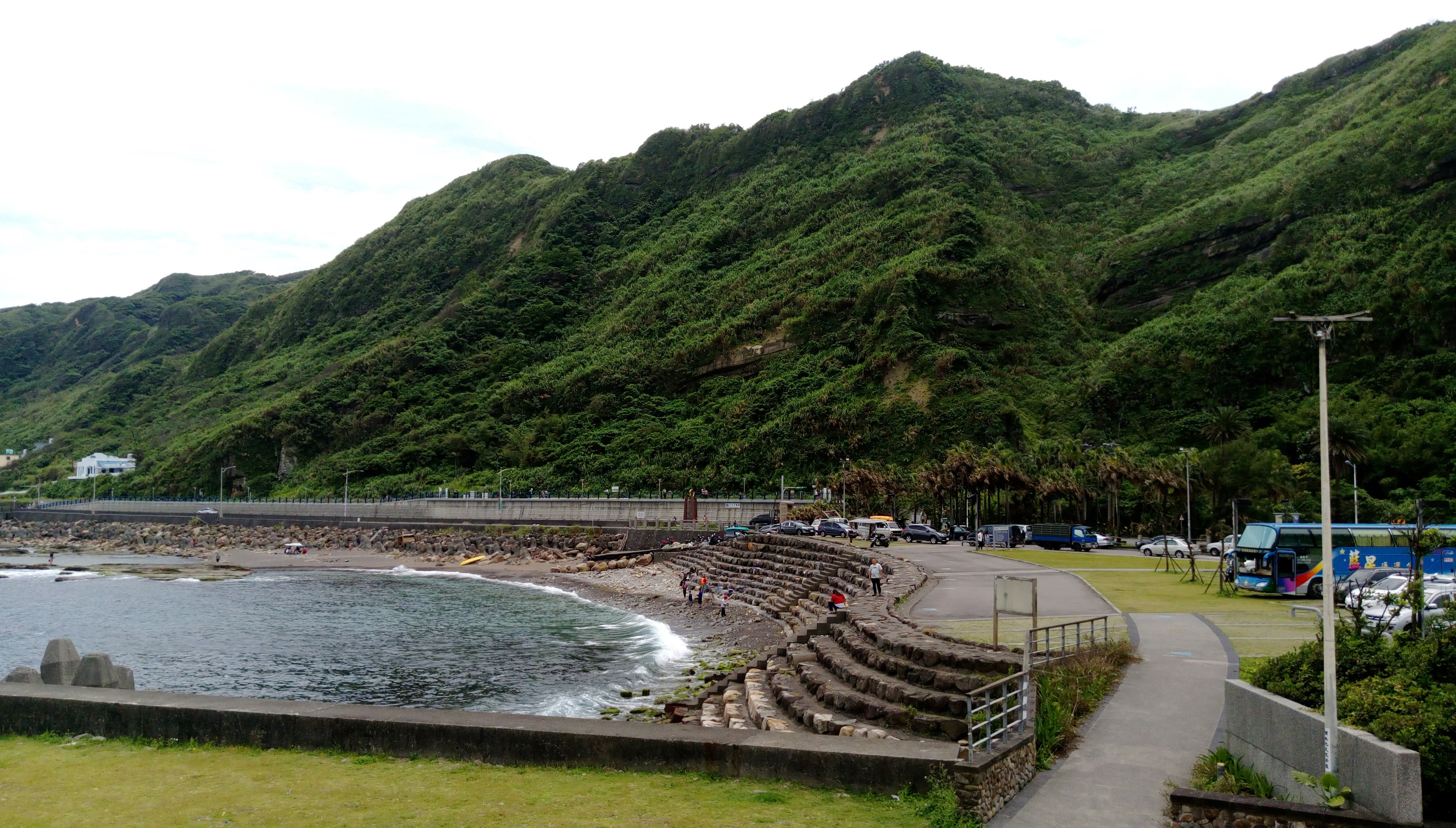 綠色山丘、石階步道、海岸線與海灣，遊客在岸邊活動