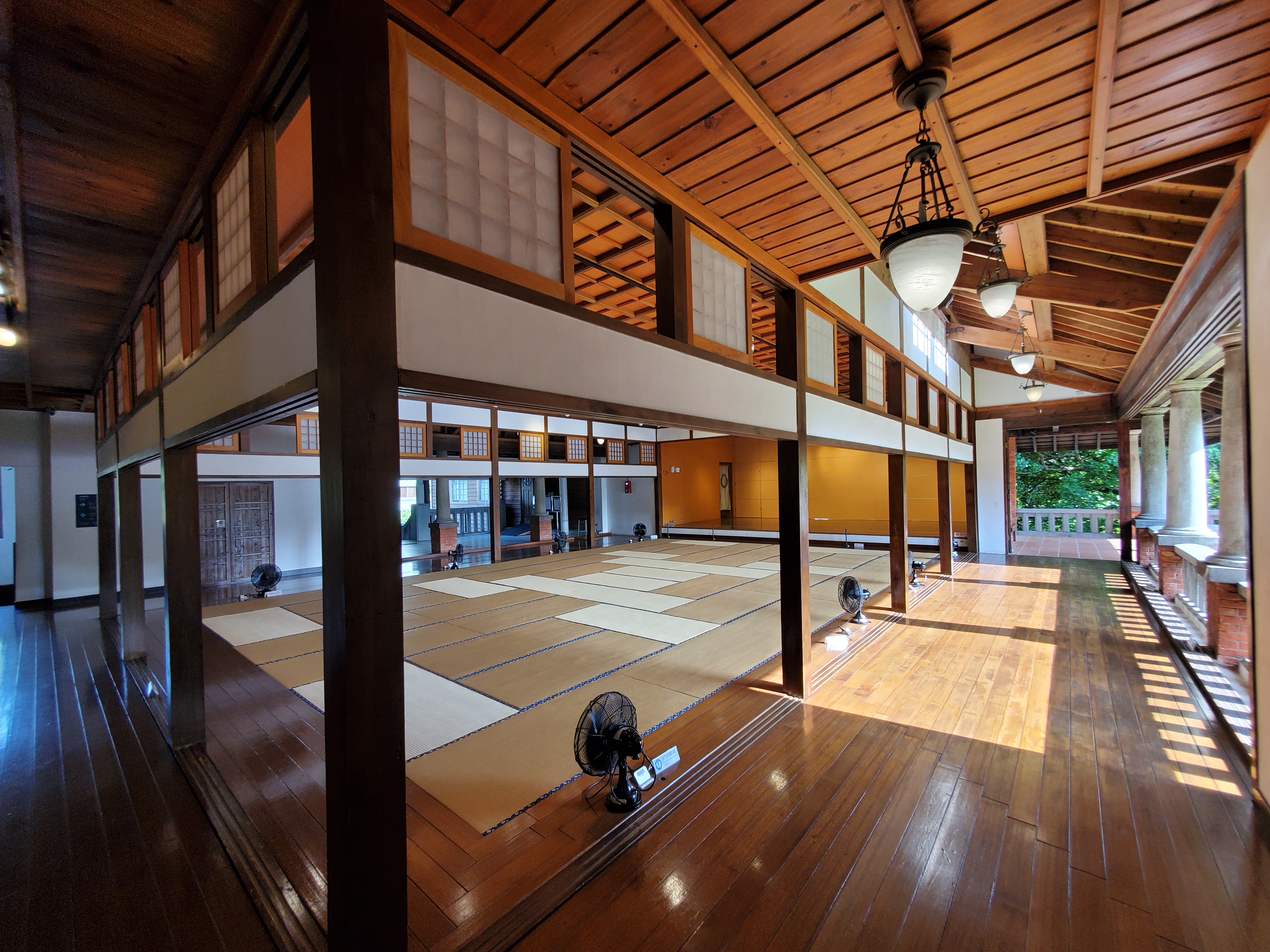 這張圖片主要展示一間具有日式風格的室內空間，鋪有榻榻米地板，周圍有木質結構與拉門，環境寬敞明亮，並擺放數台電風扇，沒有明顯浮水印。