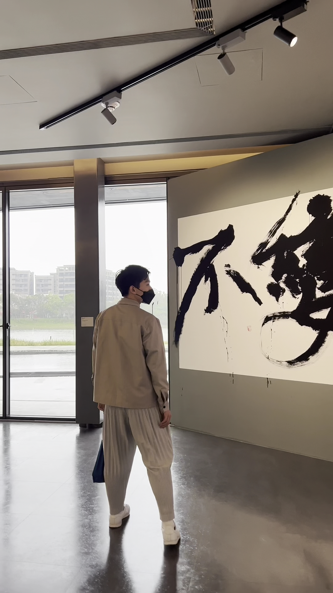 參觀者站在畫廊內欣賞大型書法藝術作品與窗外水景