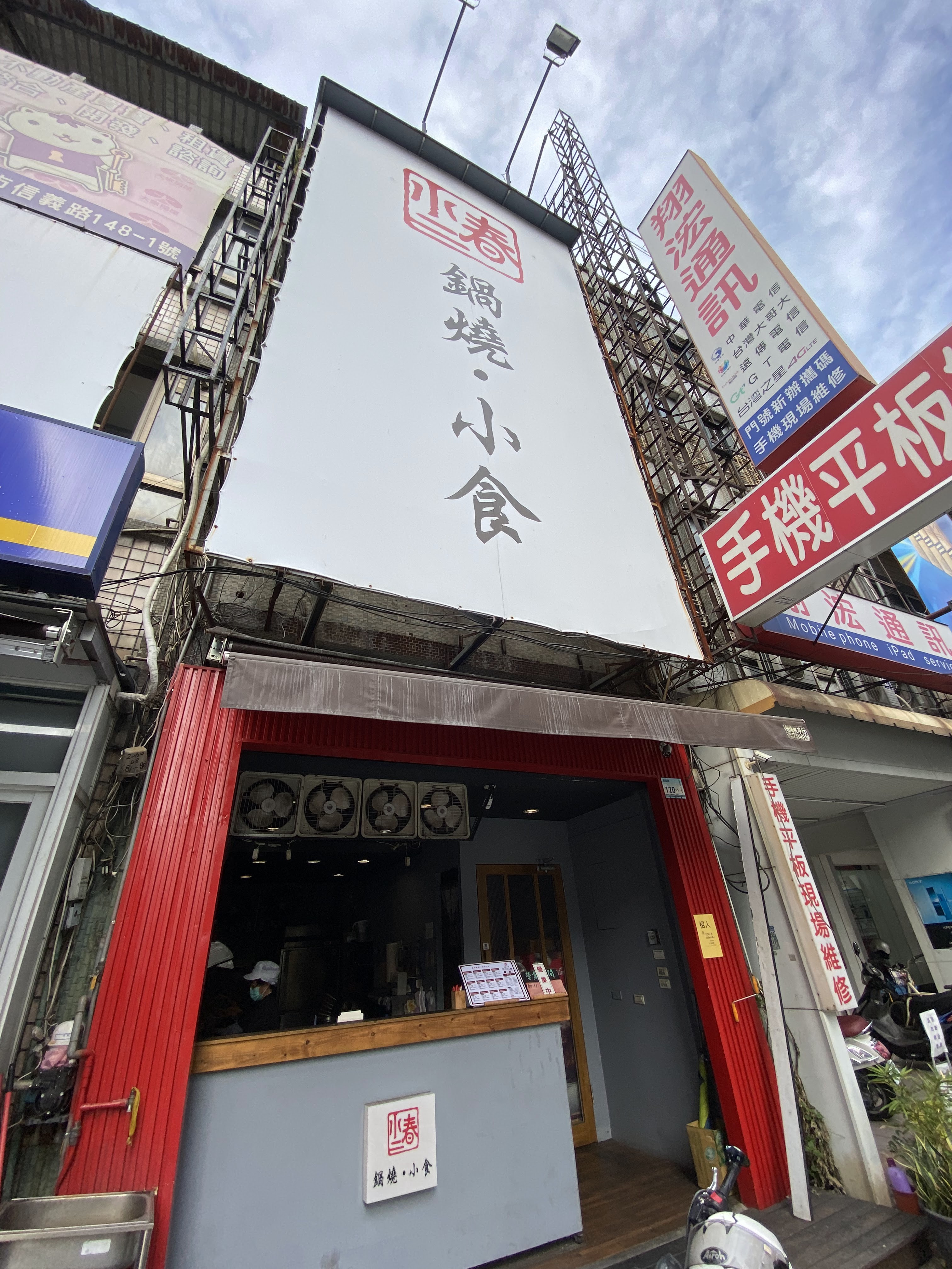 這張圖片主要是一家名稱為『四春鍋燒小食』的餐飲店門口,店面以紅灰配色為主,上方有大招牌。圖片未見明顯浮水印。