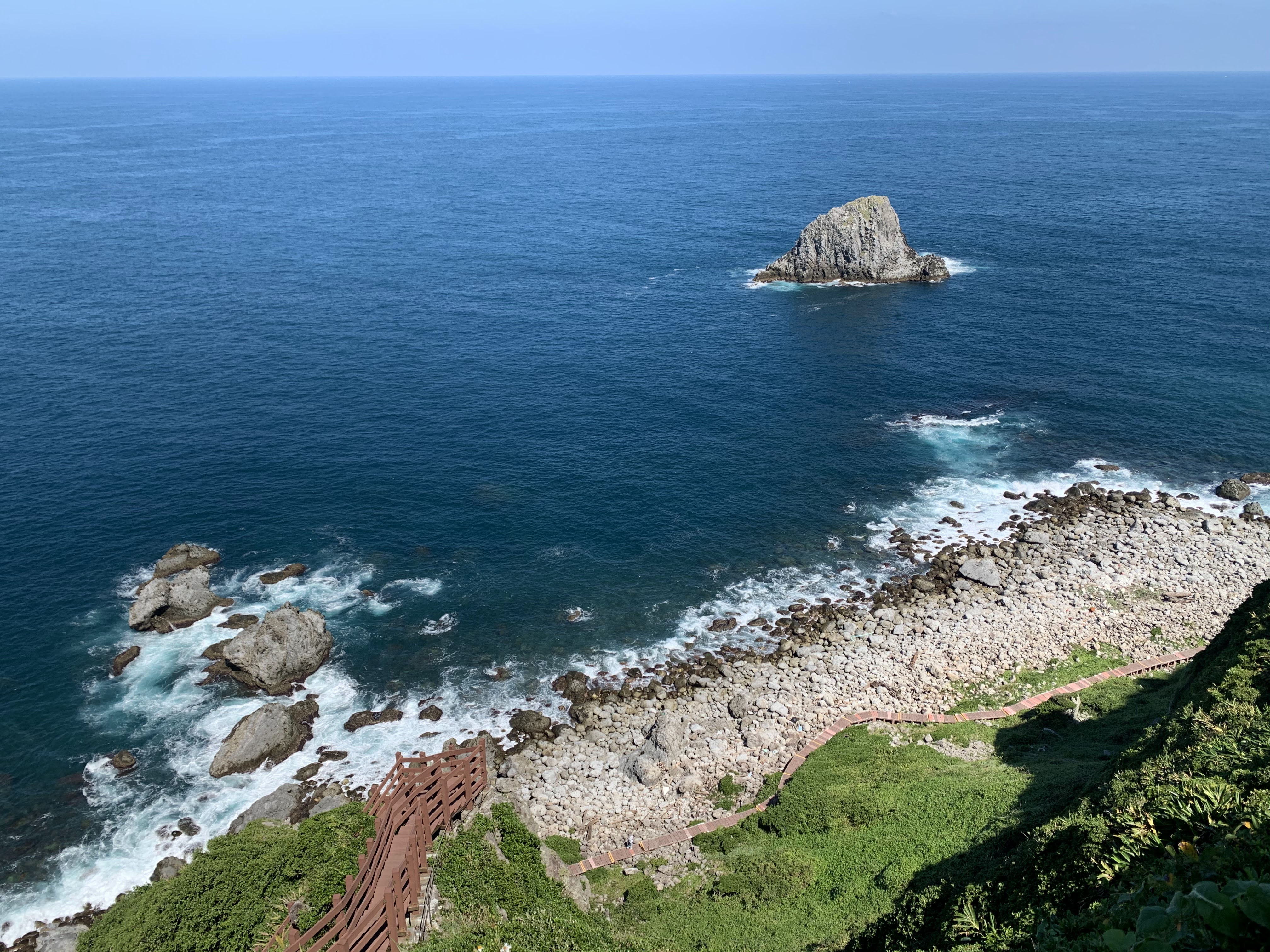 海中巨石與浪花拍打海岸，沿岸有步道延伸