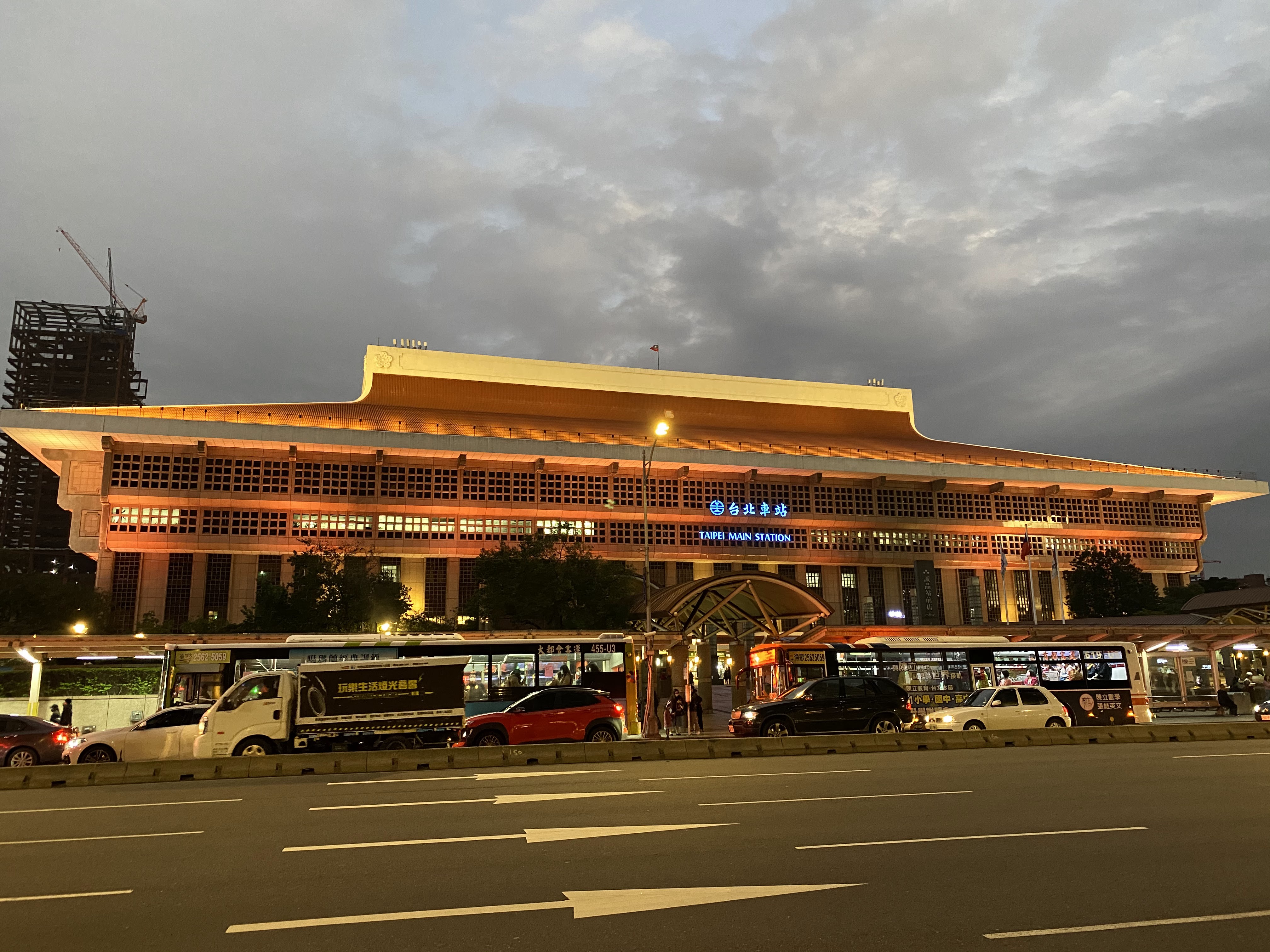 台北車站夜景，建築外觀亮燈，前方有公車與汽車