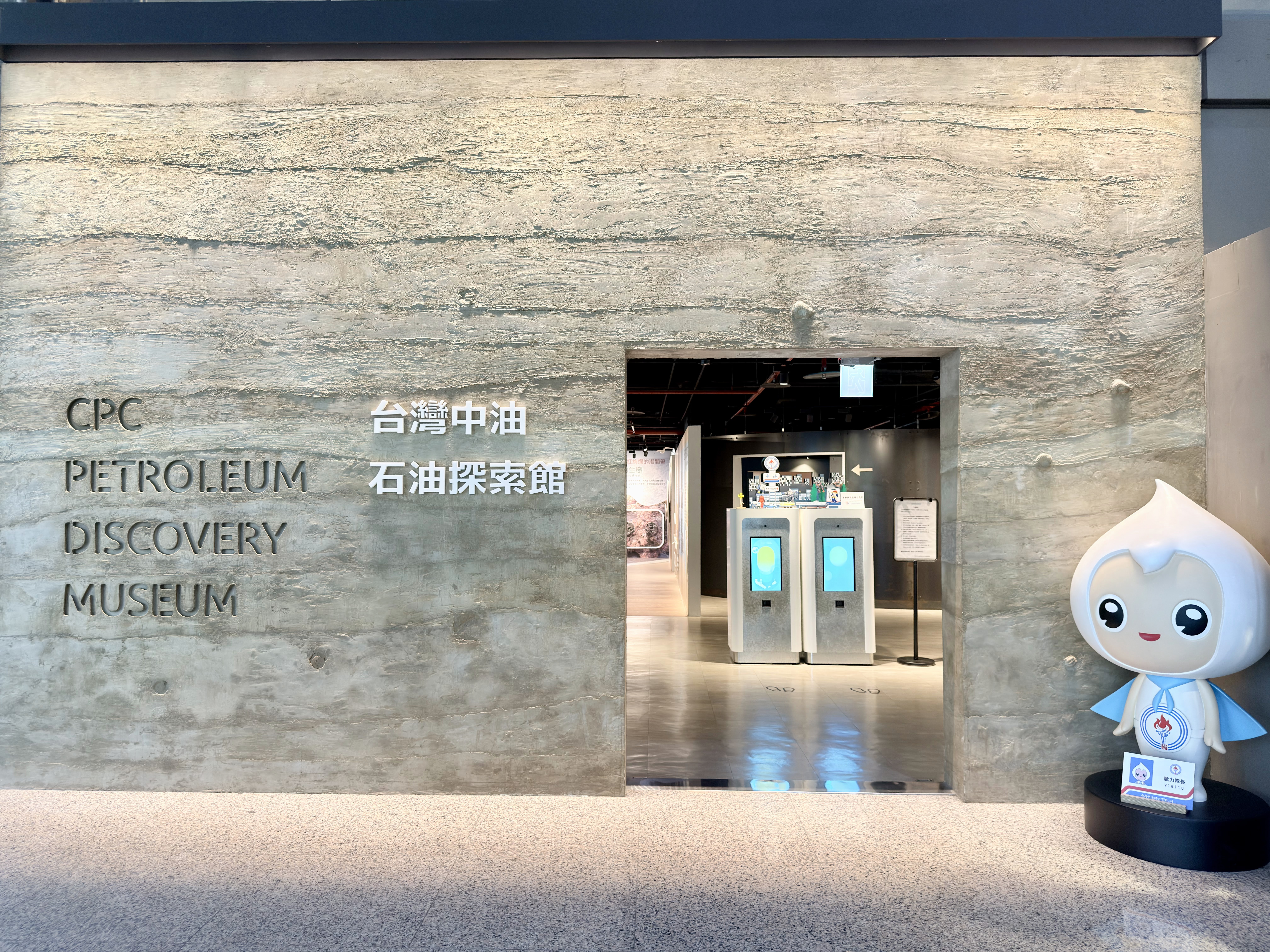 這張圖片主要展示了台灣中油石油探索館的入口，左側有中英文館名，右側有一個可愛吉祥物立牌，內部明亮現代，沒有浮水印。