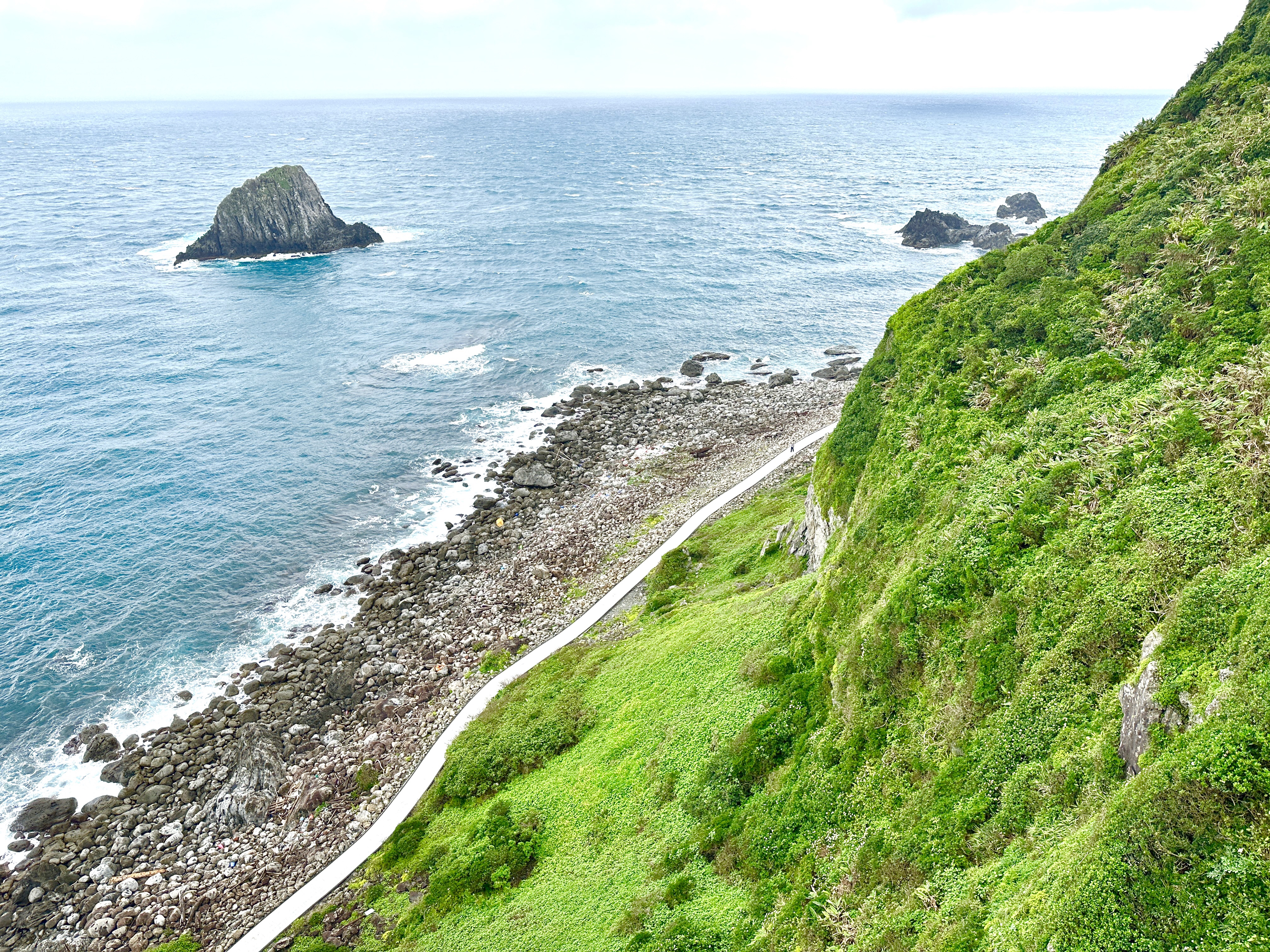 碧藍海洋與右側陡峭山坡，下方可見步道