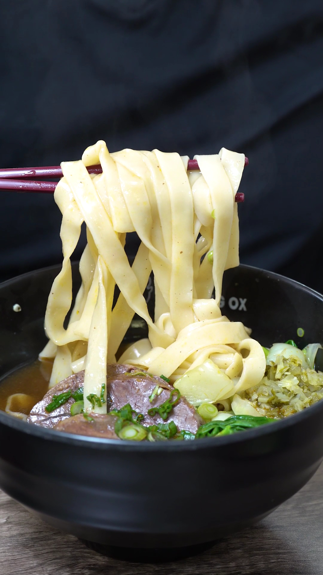 這張圖片主要是一碗牛肉麵,有寬麵條、牛肉塊、蔥花與青菜,湯底看起來濃郁美味,上面看不見浮水印。