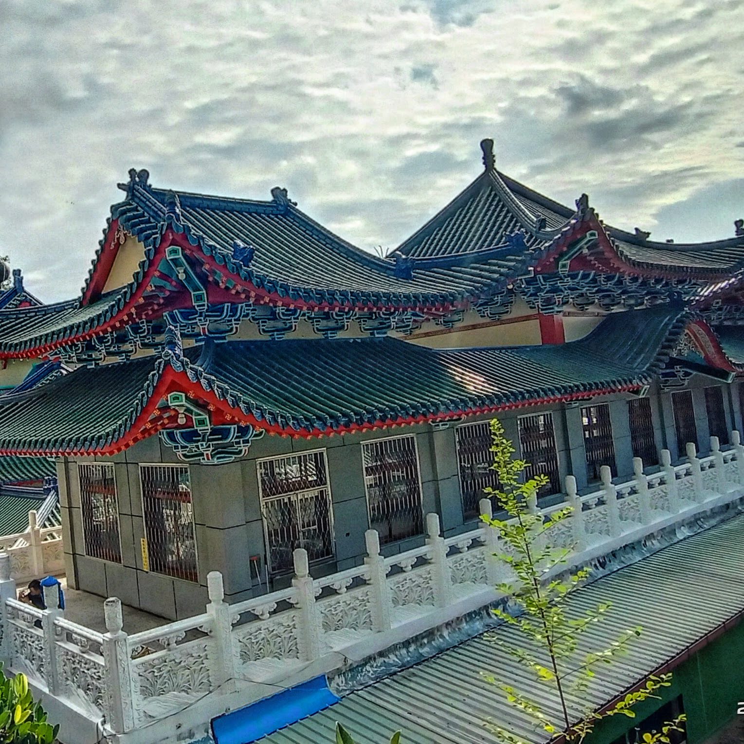 這張圖片展示了一座具有傳統中國建築風格的寺廟或廟宇。屋頂採用綠色瓦片,屋脊和簷口則以鮮紅色與藍色裝飾,建築裝飾精美,下方有白色石欄杆。圖片無明顯浮水印。
