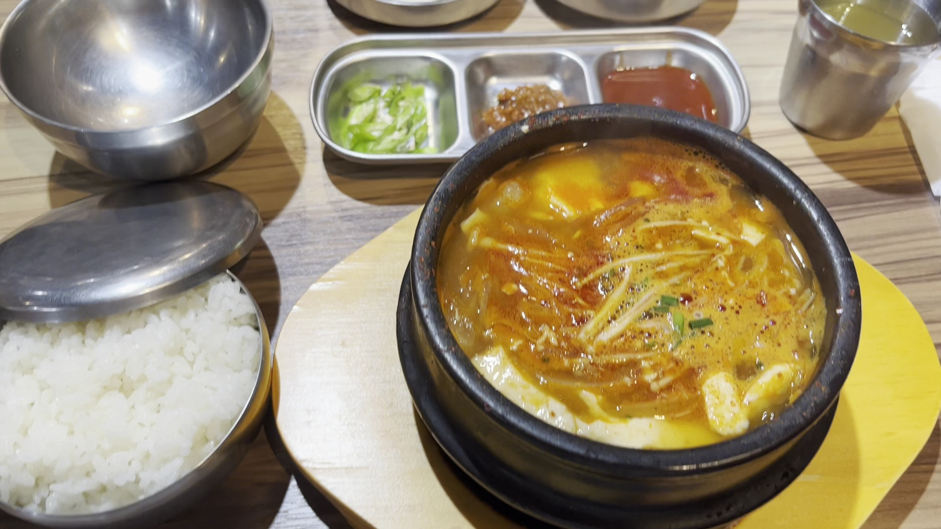 這張圖片主要是一份韓式料理,包括石鍋盛裝的湯、白飯、不鏽鋼餐具和三格小菜盤。畫面中沒有明顯的浮水印。
