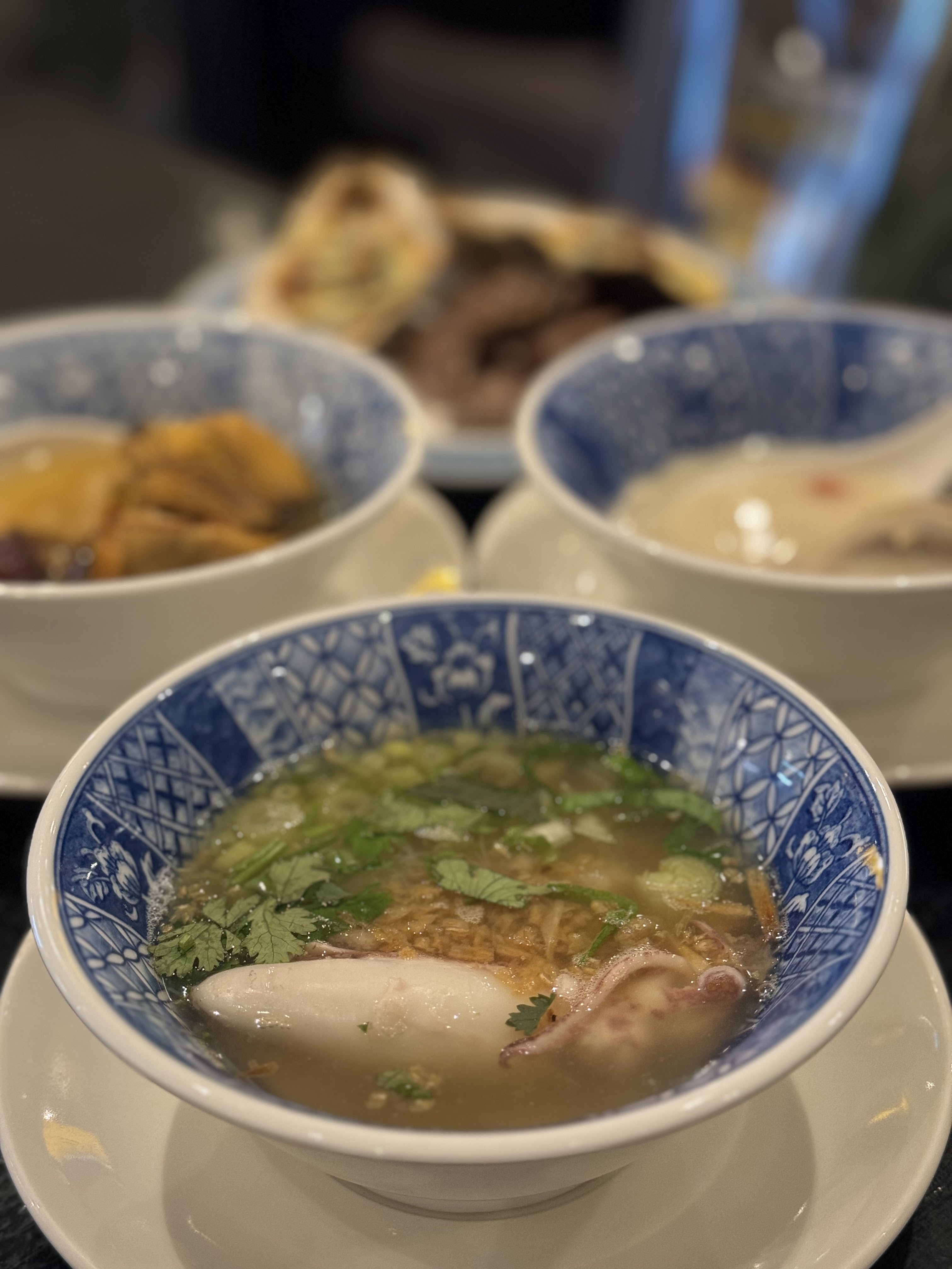 這張圖片主要展示三碗中式湯品，前方清楚可見一碗有花枝和香菜的湯，後方還有其他不同料理。圖片無明顯浮水印。