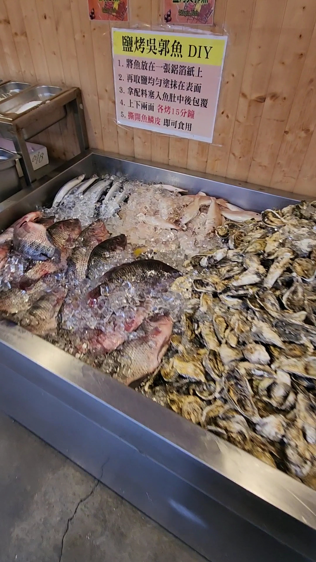 冰上新鮮魚類和牡蠣，旁邊有DIY鹽烤吳郭魚步驟牌