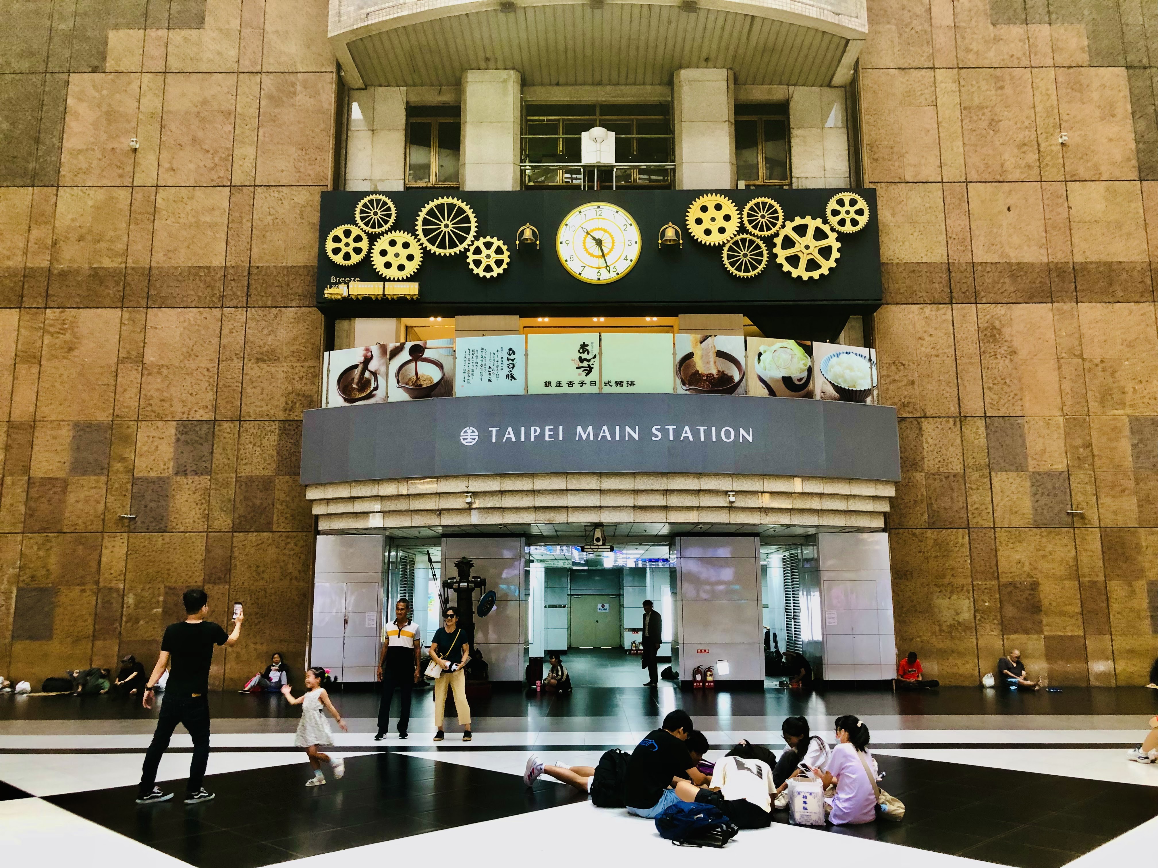 台北車站大廳，有大型時計、齒輪裝飾與Taipei Main Station字樣