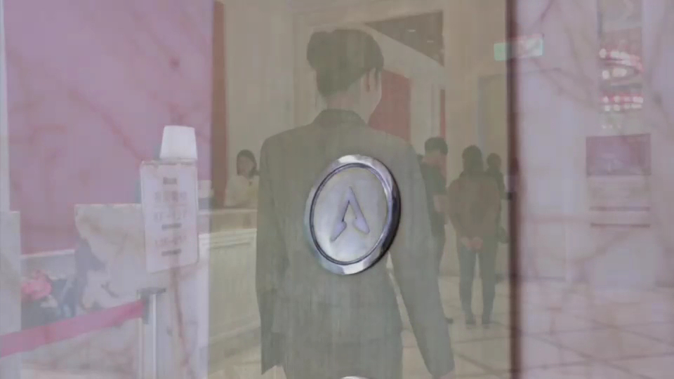 圖片主要顯示一個電梯按鈕,玻璃反射出一位穿著西裝的女性背影,還有幾位人在大廳內。未見浮水印。