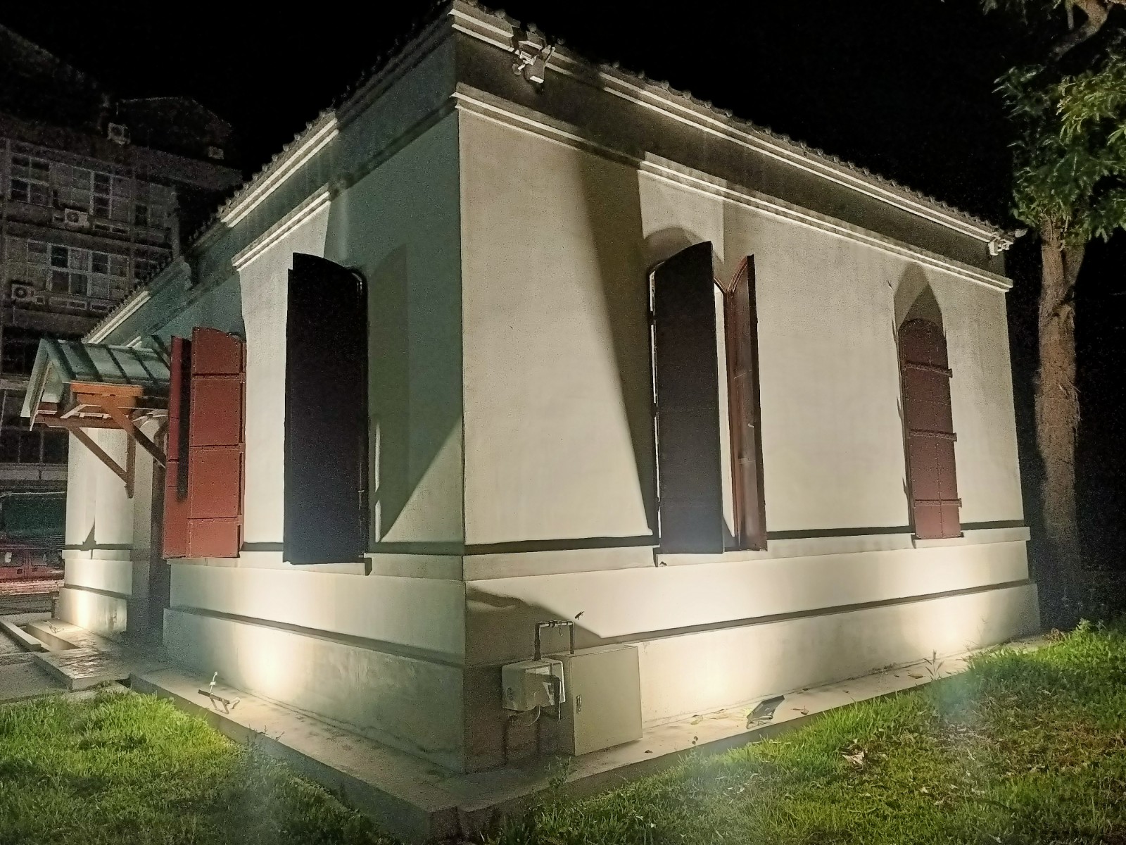 一棟白色外牆、紅色窗戶的老建築,夜間有照明燈光打亮牆面