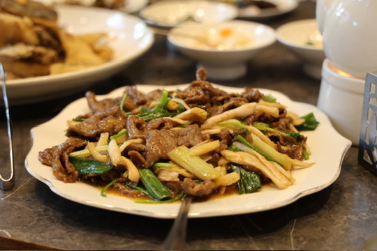 欣葉鐘菜炒牛肉搭配蔥段與杏鮑菇,背景呈現豐盛桌菜氛圍
