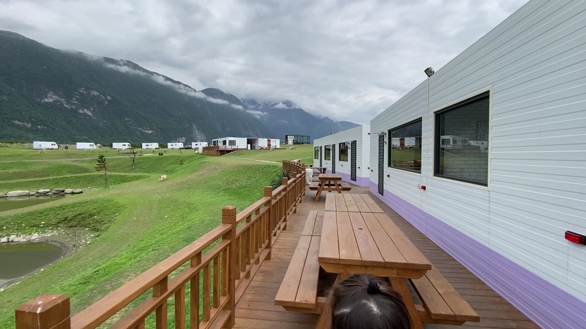 坐落於山景與草地間的露營區,有白色建築、木製露台與野餐桌