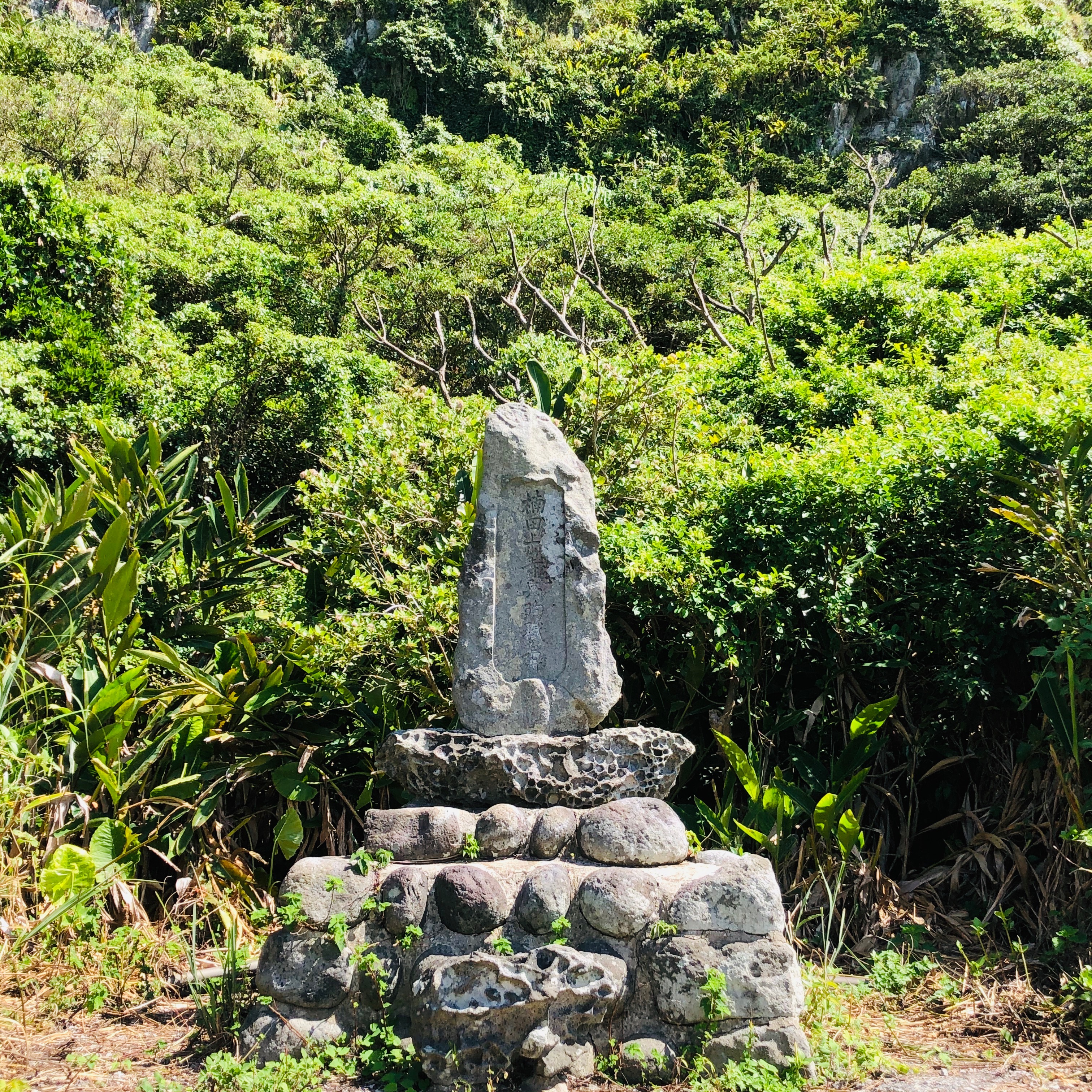 石碑立於多層圓形石塊基座上，背景是綠色山坡