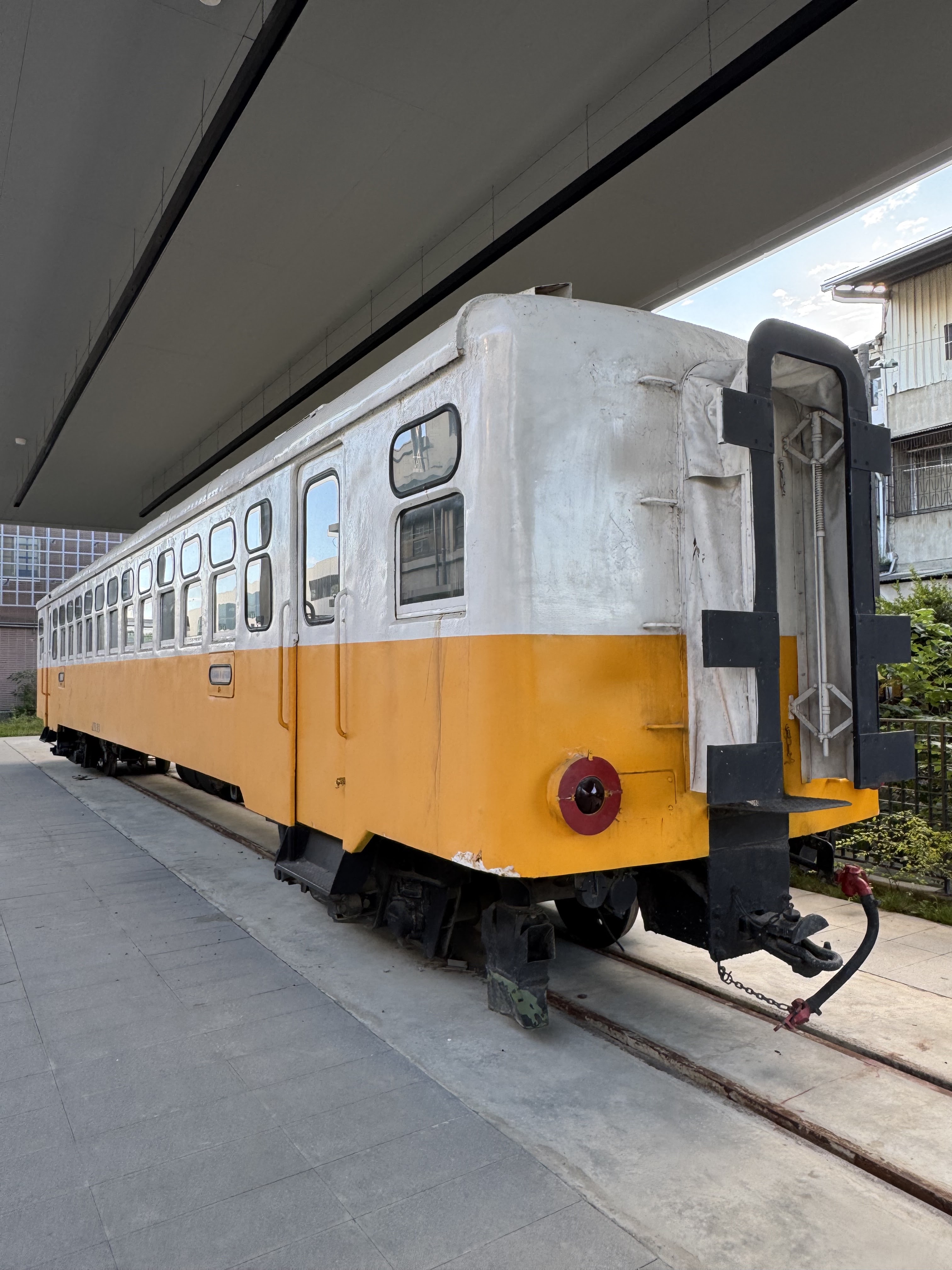 停放於軌道上的橘白色老式火車車廂，背景有現代建築與住宅。