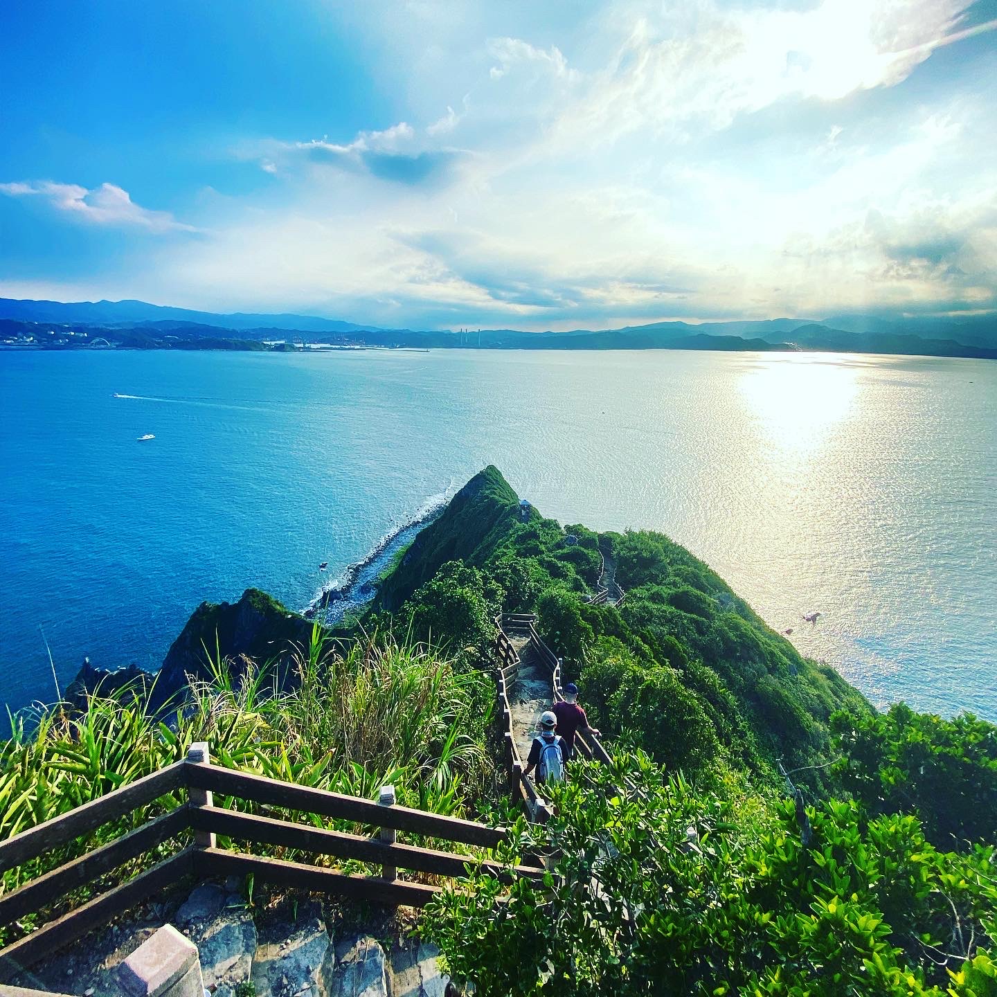 通往山頂的小路與遠方蔚藍海面，前景有遊客步行