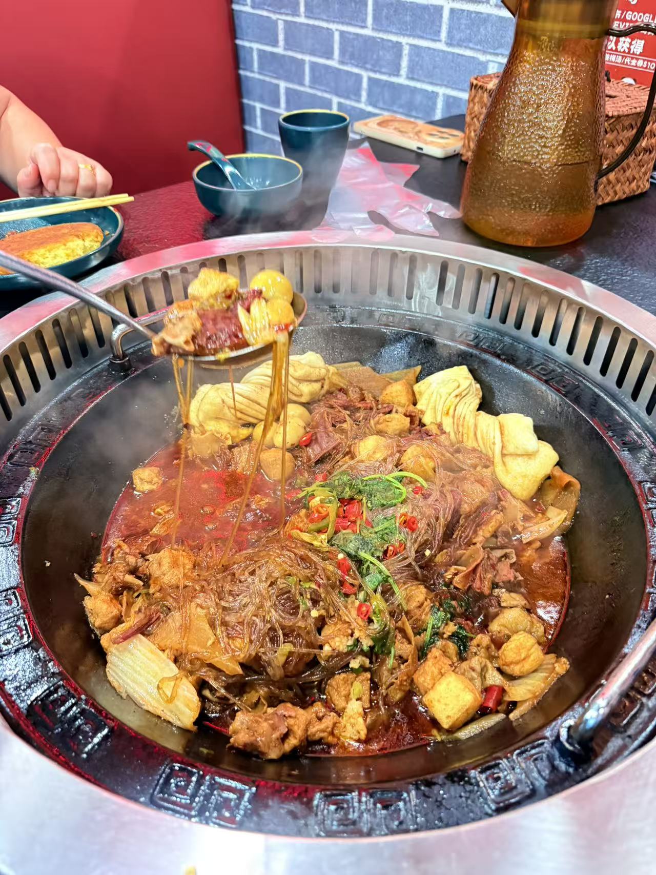 這張圖片主要是一鍋豐富的麻辣火鍋,裡面有粉絲、蔬菜、豆腐、肉片和辣椒等食材,紅湯看起來麻辣誘人,整體氣氛溫馨熱鬧。圖片沒有明顯浮水印。