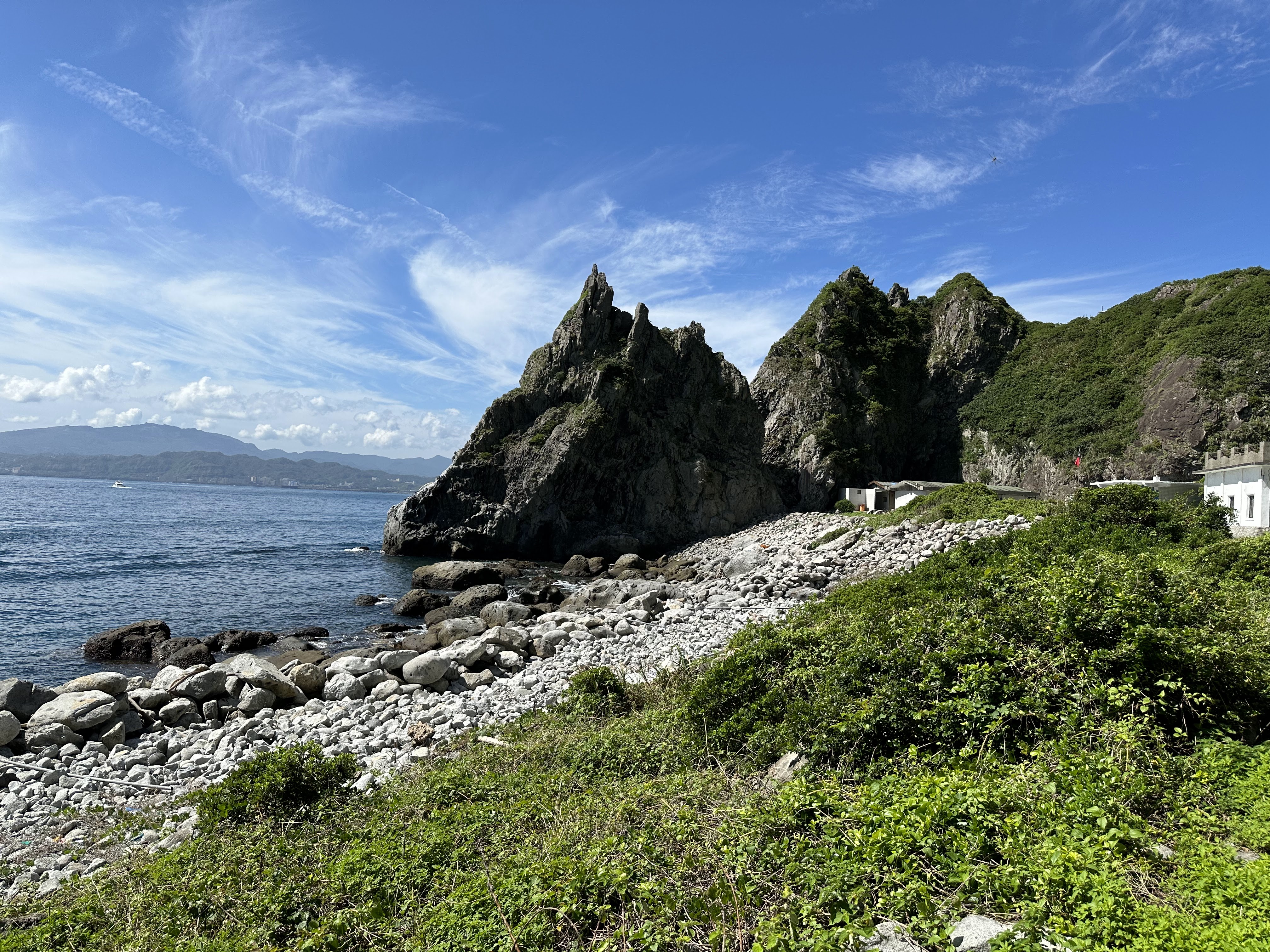 礫石灘前方是岩石山峰與海面，右側可見建築物