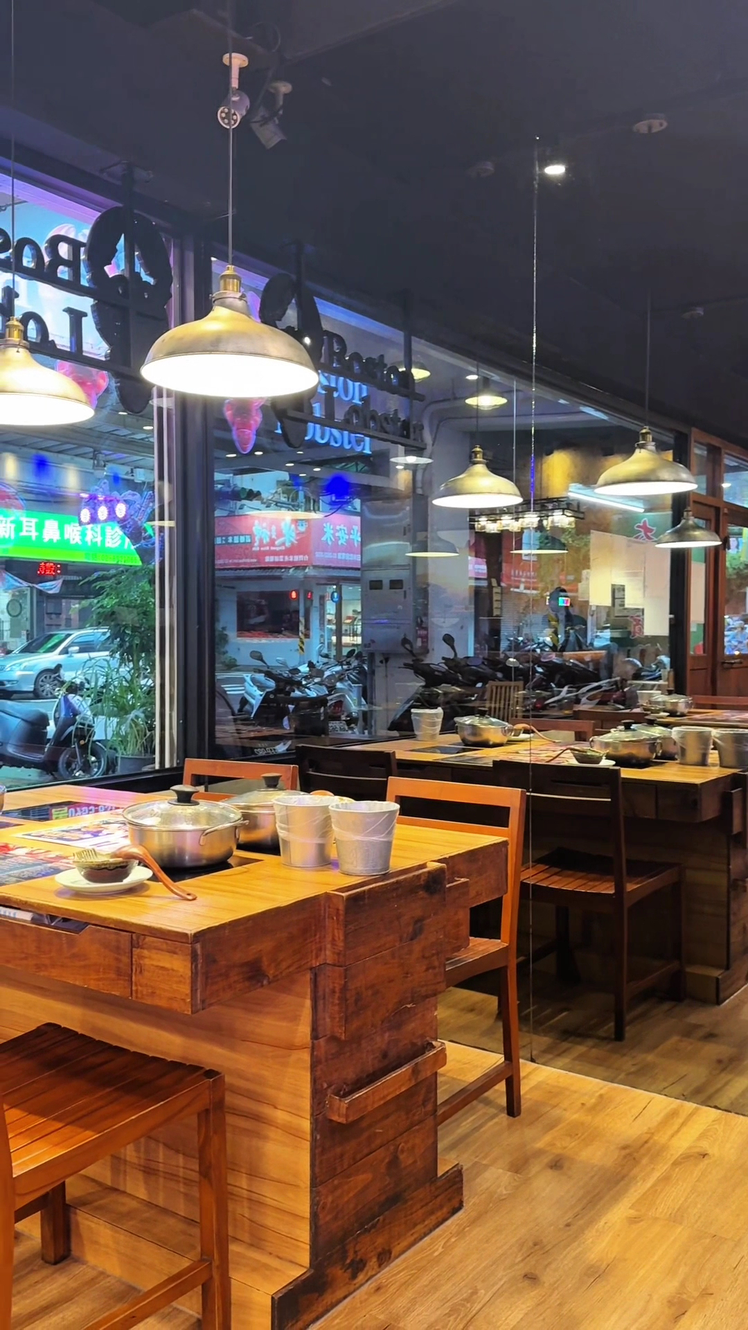 這張圖片主要顯示一家餐廳的內部景象,有木質餐桌椅和餐具擺設,桌上有火鍋和水桶,窗外可以看到街景與招牌。圖片沒有明顯浮水印。