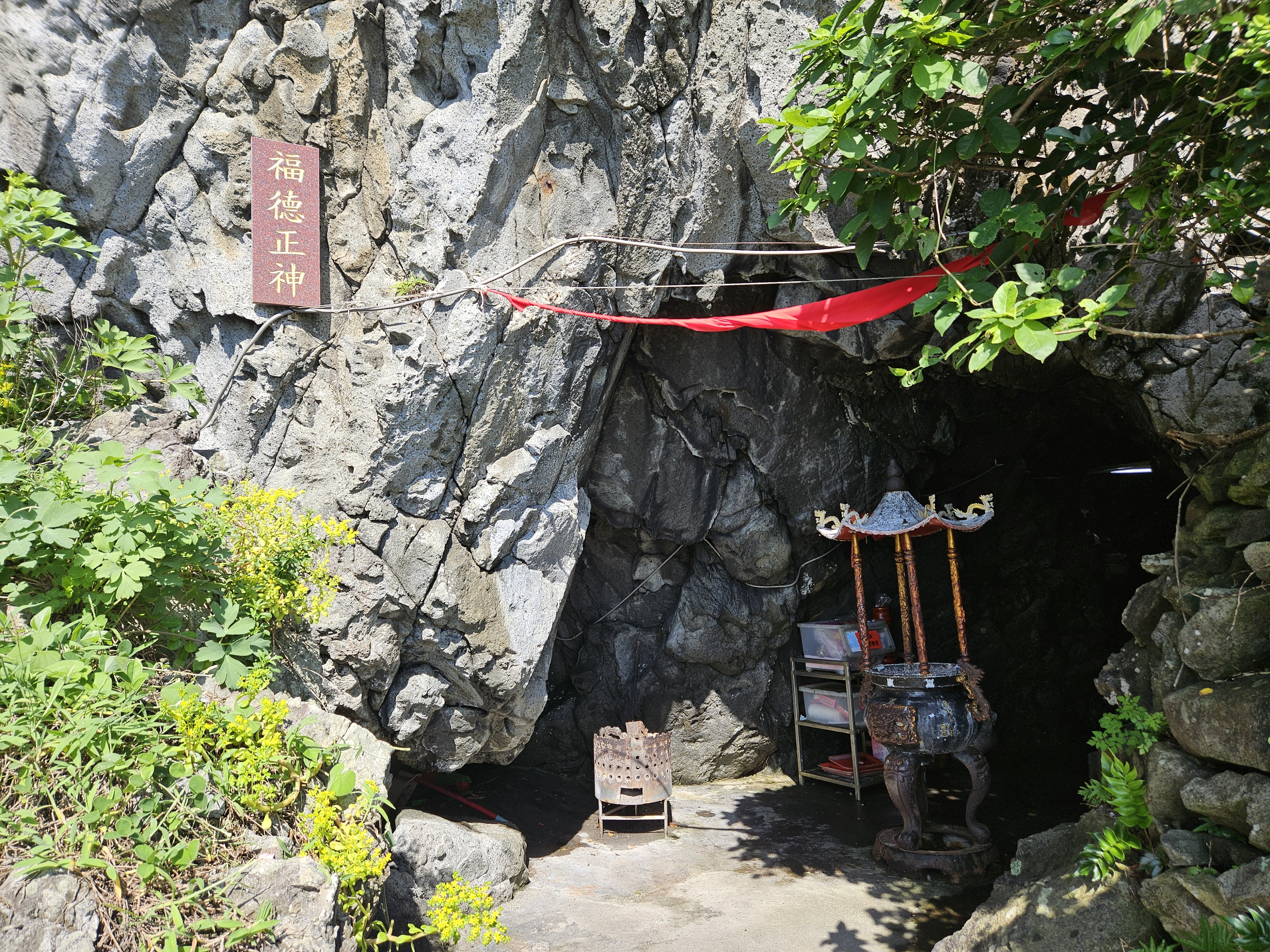 岩石洞口中的小型土地公廟，前方有香爐與祭祀用品