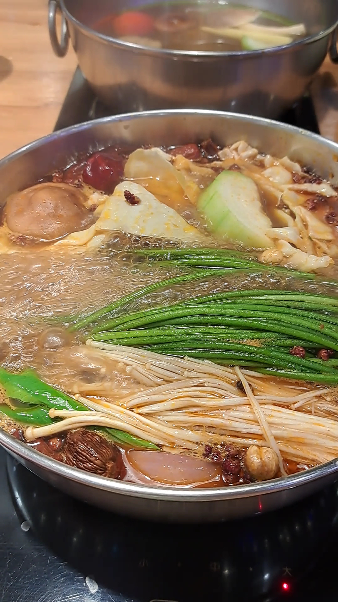 這張圖片主要是火鍋,湯底紅亮,裡面有金針菇、豆皮、蔬菜、香菇、鴨血及青蔥等食材,正在火爐上煮沸。圖片沒有浮水印。
