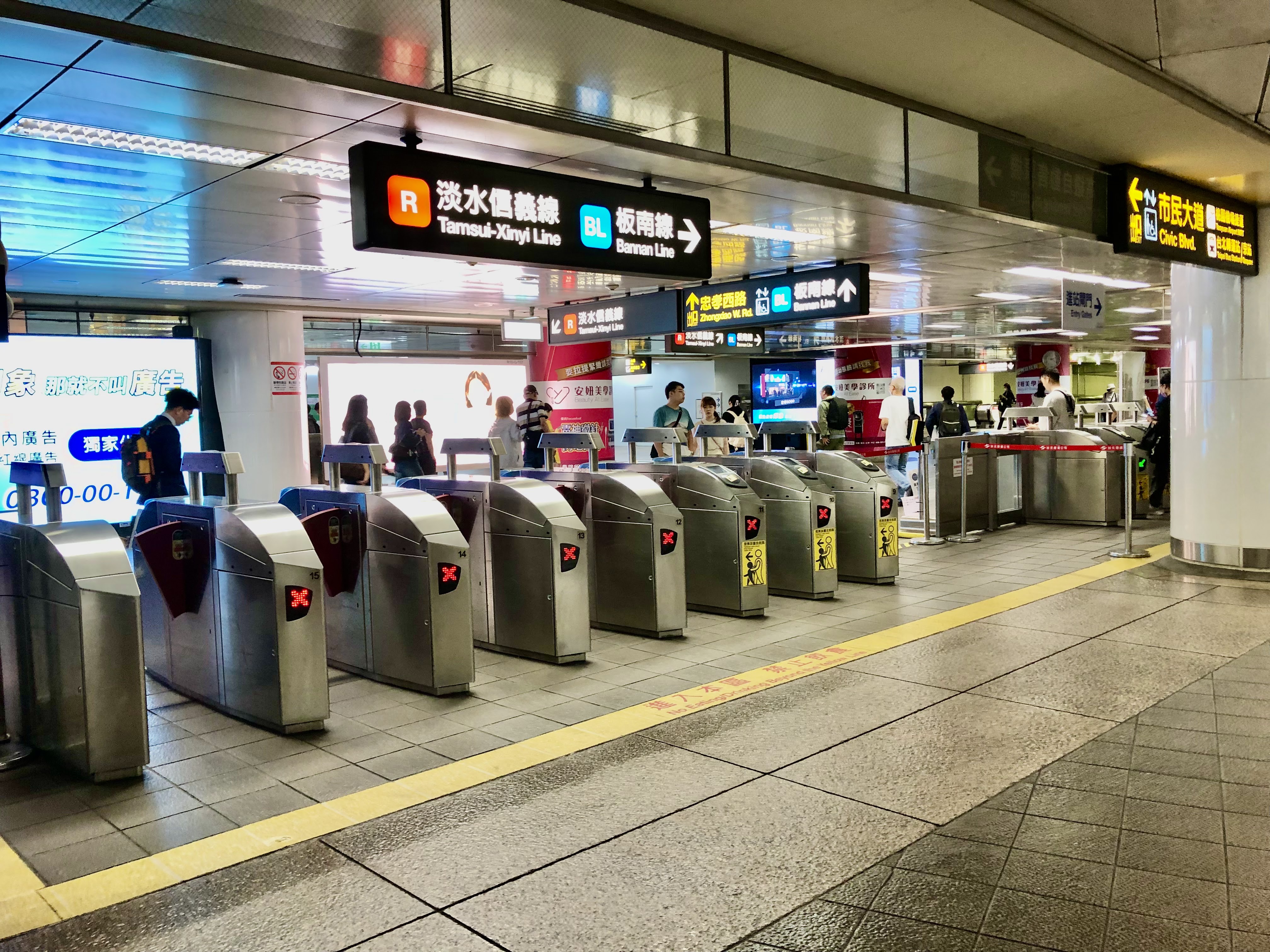 台北捷運車站閘門區域，有多條路線指示牌與電子廣告看板