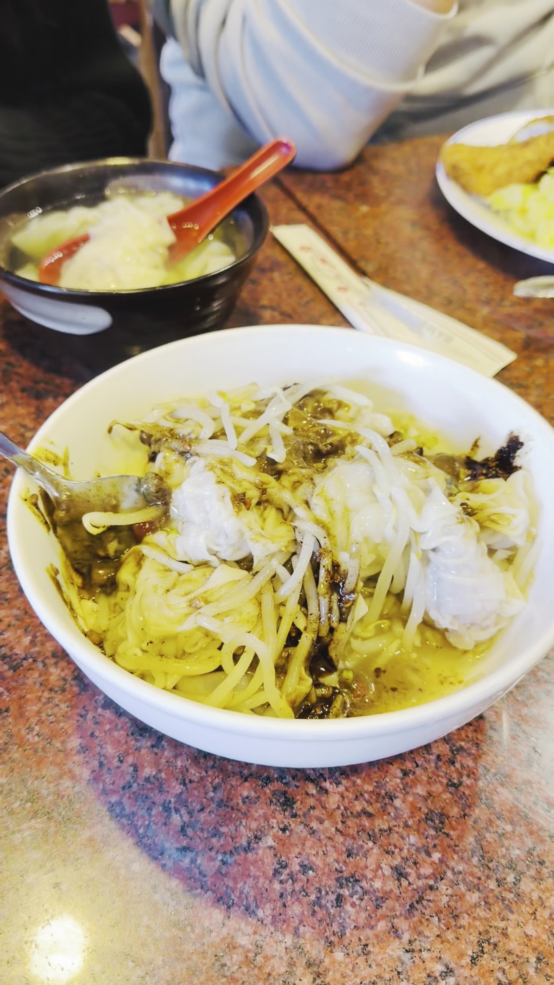 這張圖片主要有一碗淋上醬料和豆芽菜的腸粉,旁邊還有一碗湯品和其他食物,桌面上有筷子和湯匙,沒有明顯的浮水印。