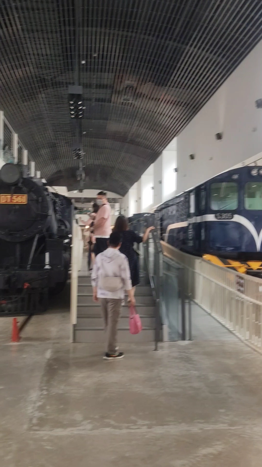 火車博物館展區，左側有一台黑色蒸汽火車，右側有藍白色柴油火車，中間有參觀的民眾行走其間。